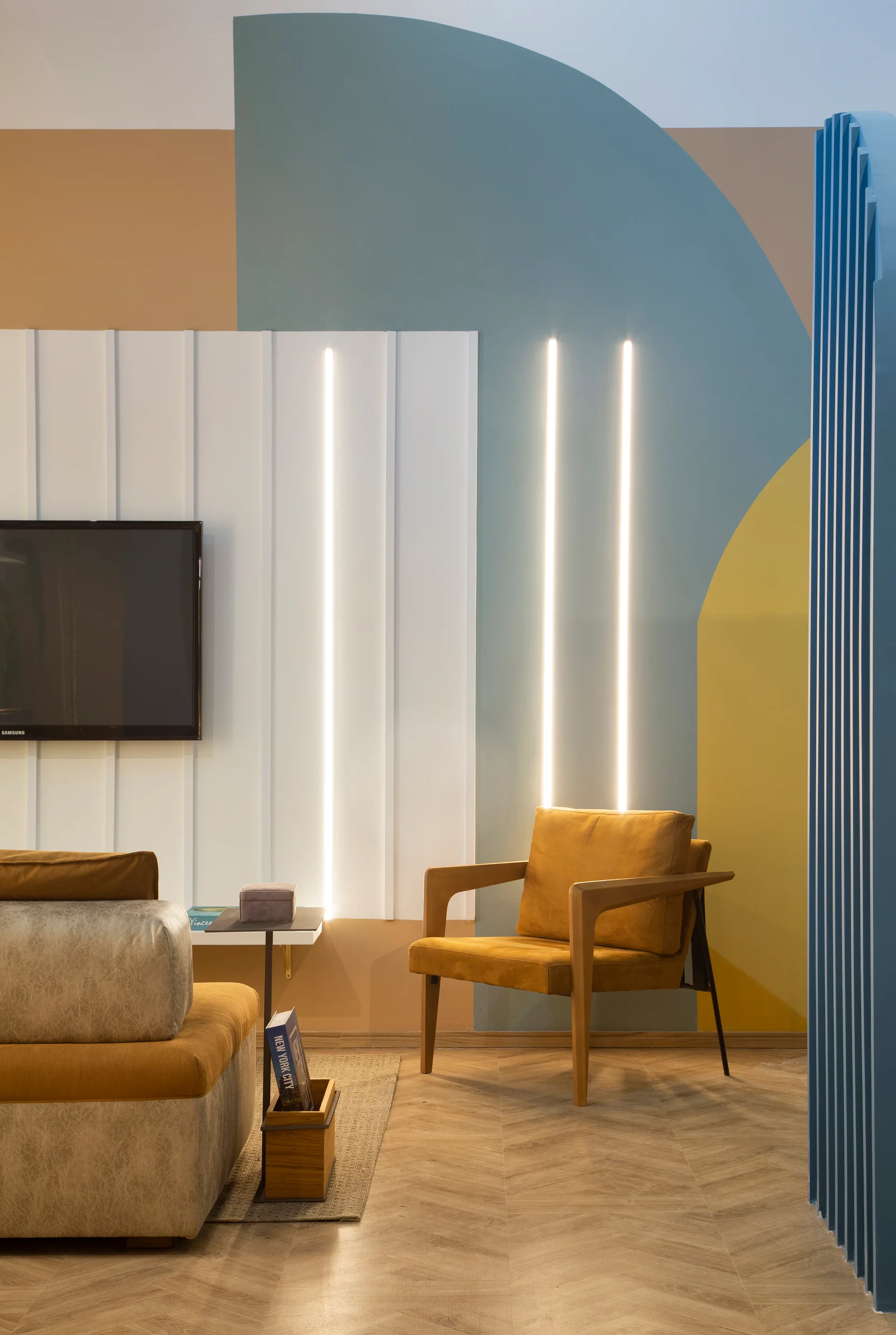 A contemporary living room features a geometric color-blocked wall with integrated vertical light strips behind a mustard yellow armchair.