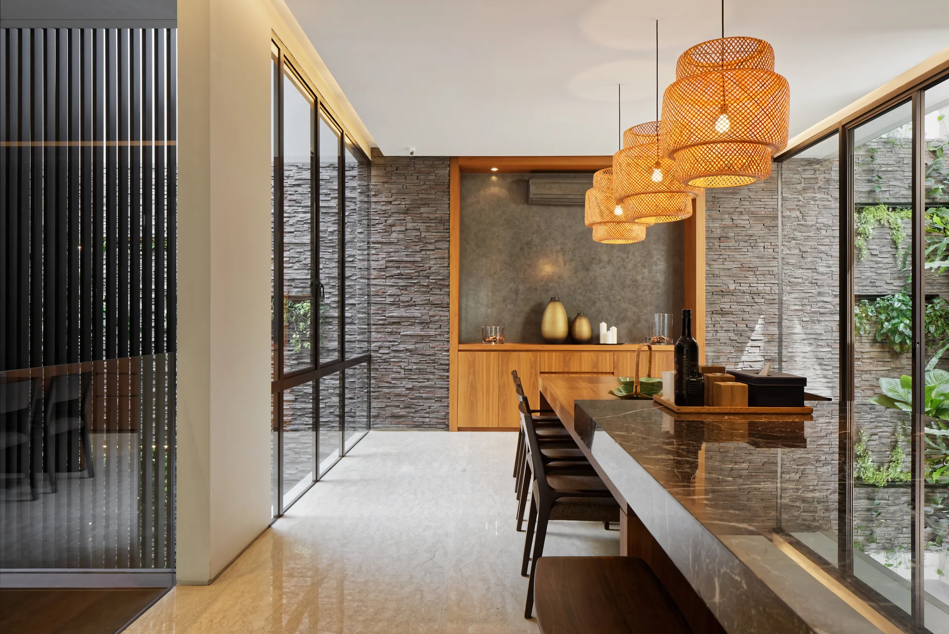 A modern kitchen with a dark marble island, three woven rattan pendant lights, wood cabinetry, and a grey stacked stone accent wall.
