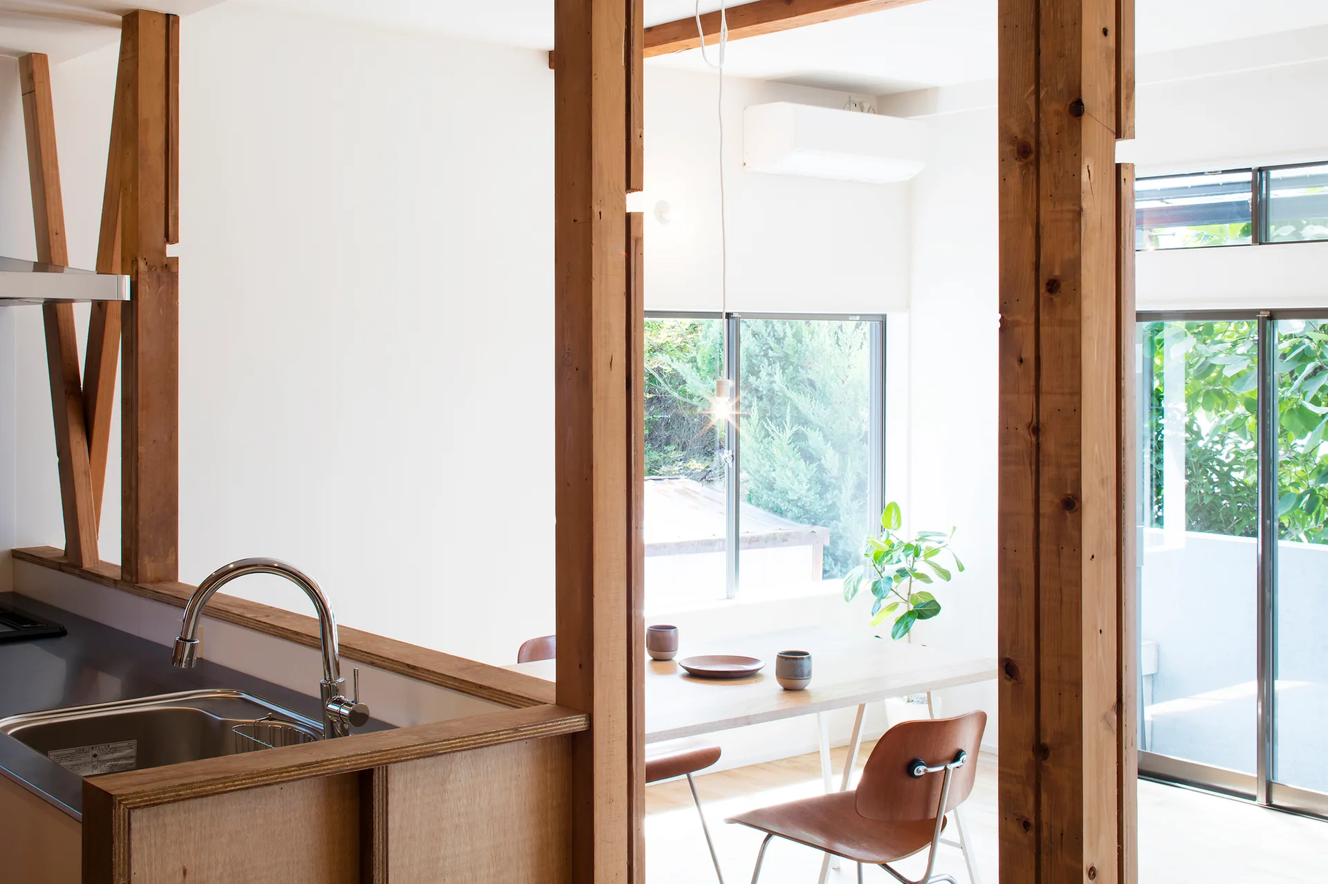 A modern open kitchen and dining area featuring structural wood posts, a stainless steel sink, and a wooden dining set under a large window.