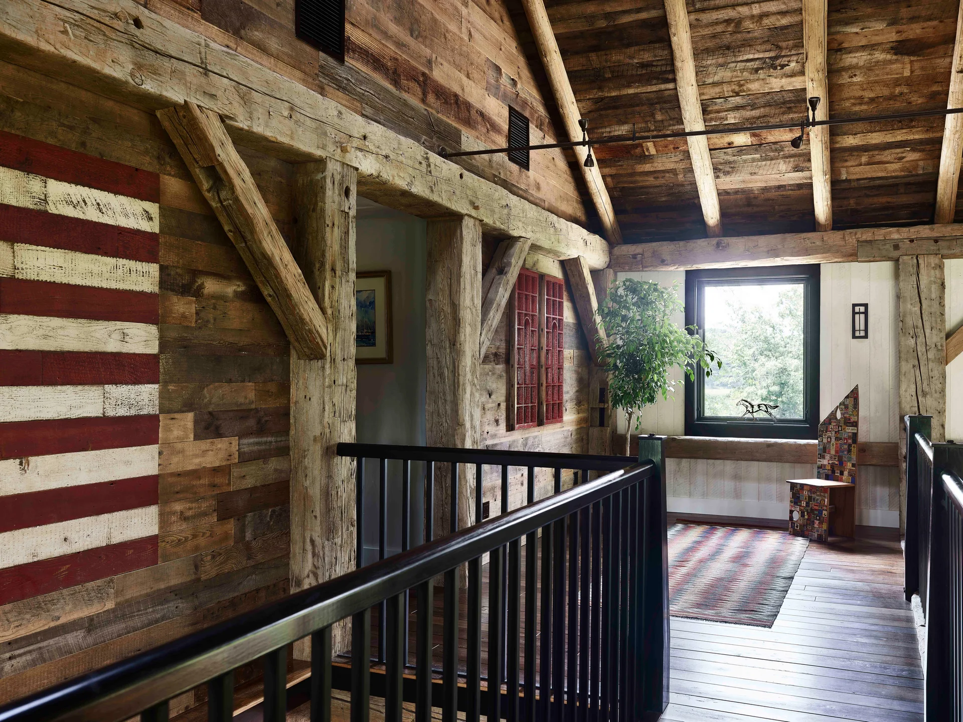 A rustic mezzanine landing features weathered wood plank walls, heavy timber columns, a black railing, and a large wooden American flag motif.