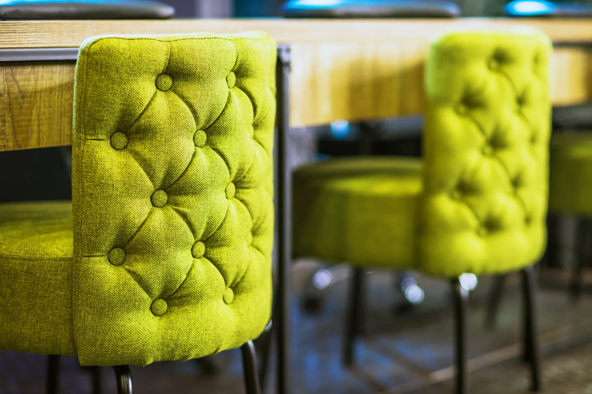 Close-up of two lime green fabric-upholstered chairs with button tufting arranged at a light wood table.