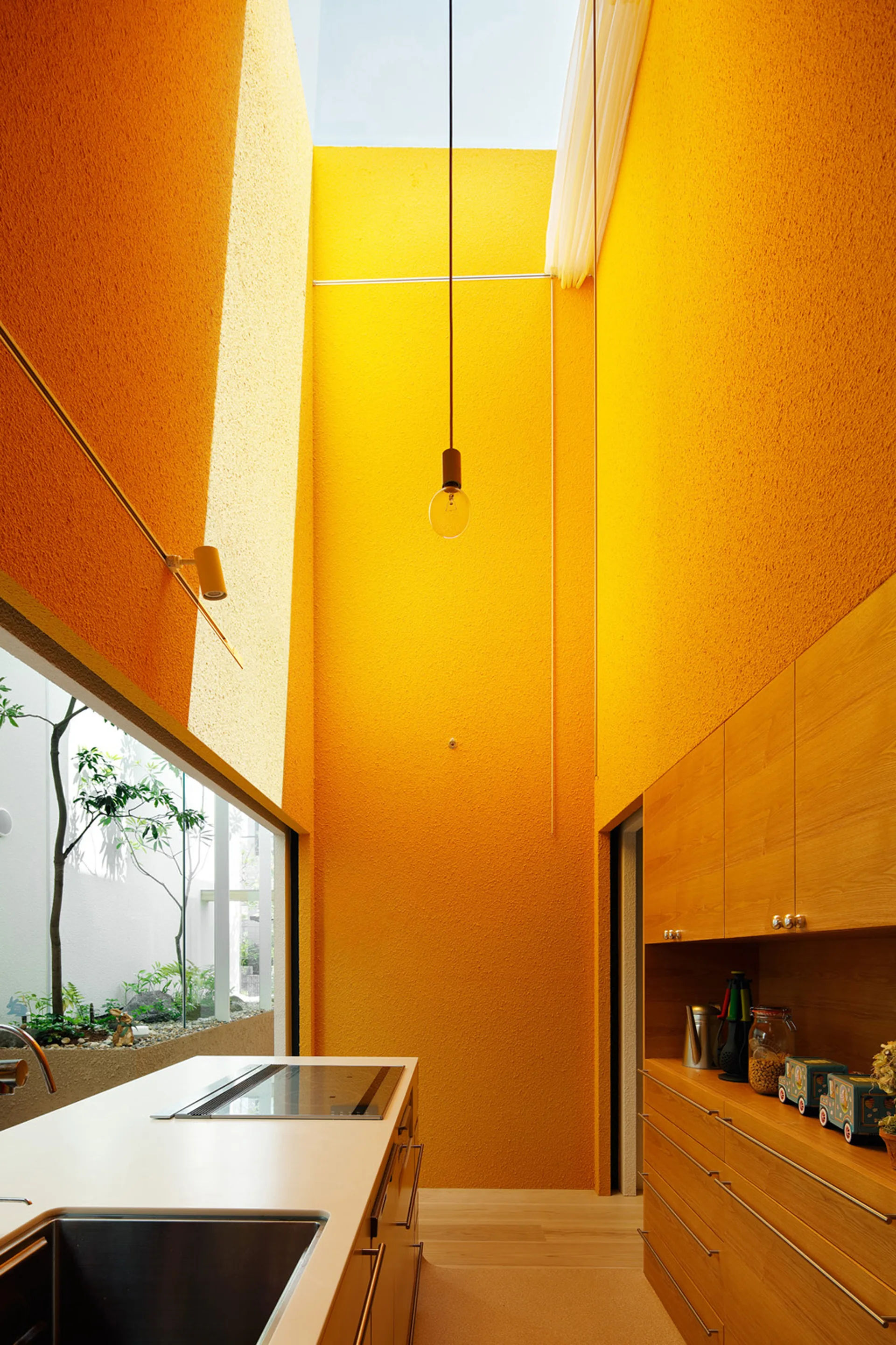 A modern kitchen with textured orange walls, a high skylight, natural wood cabinetry, and a kitchen island with a white countertop.