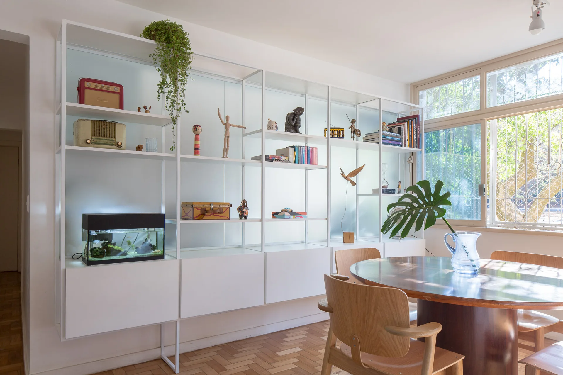 A bright dining room featuring a white modular shelving unit filled with decor next to a round wooden dining table and curved wooden chairs.