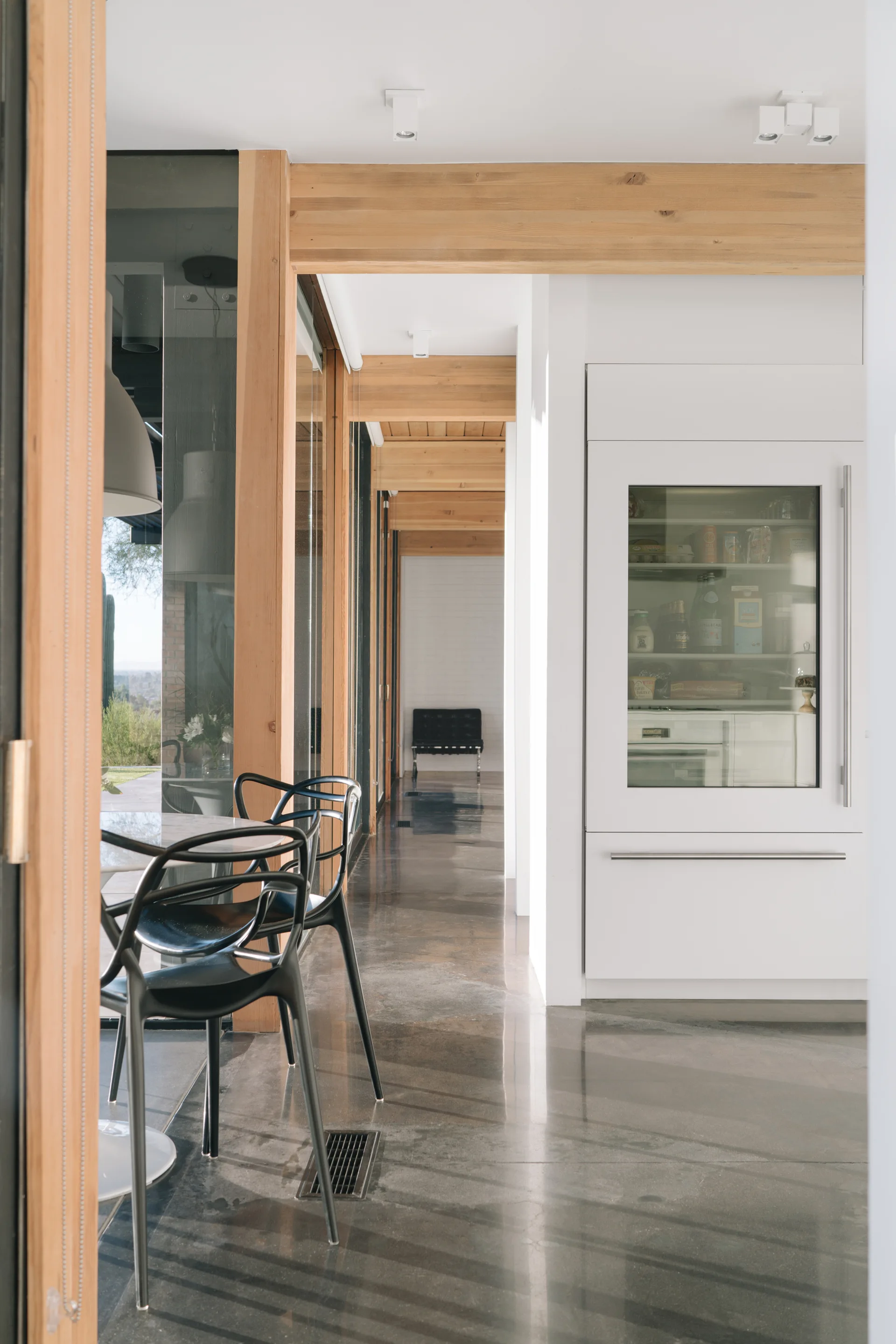 A modern kitchen hallway features exposed light wood ceiling beams, a polished concrete floor, and a white integrated glass-front refrigerator.