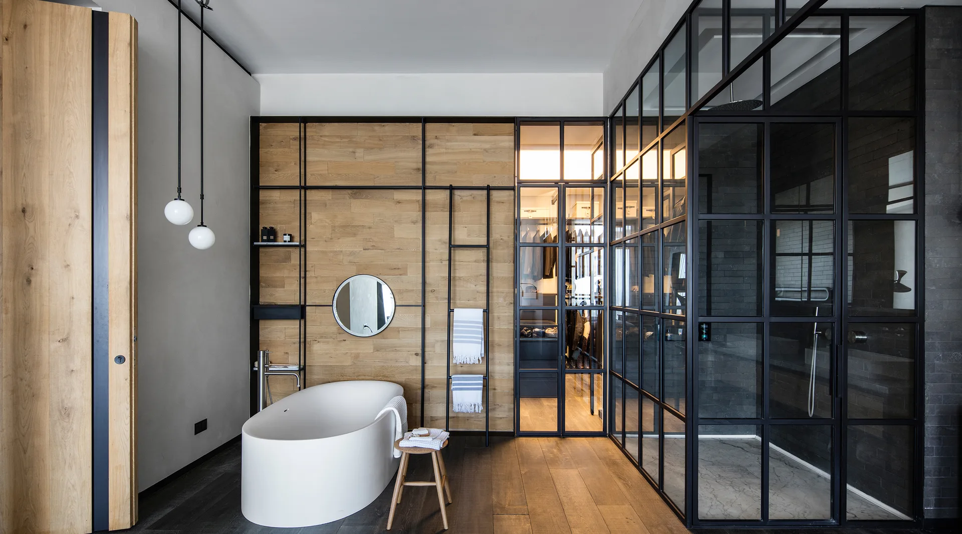 A modern bathroom featuring a white freestanding bathtub against a wood-paneled wall next to a black metal grid glass shower enclosure.