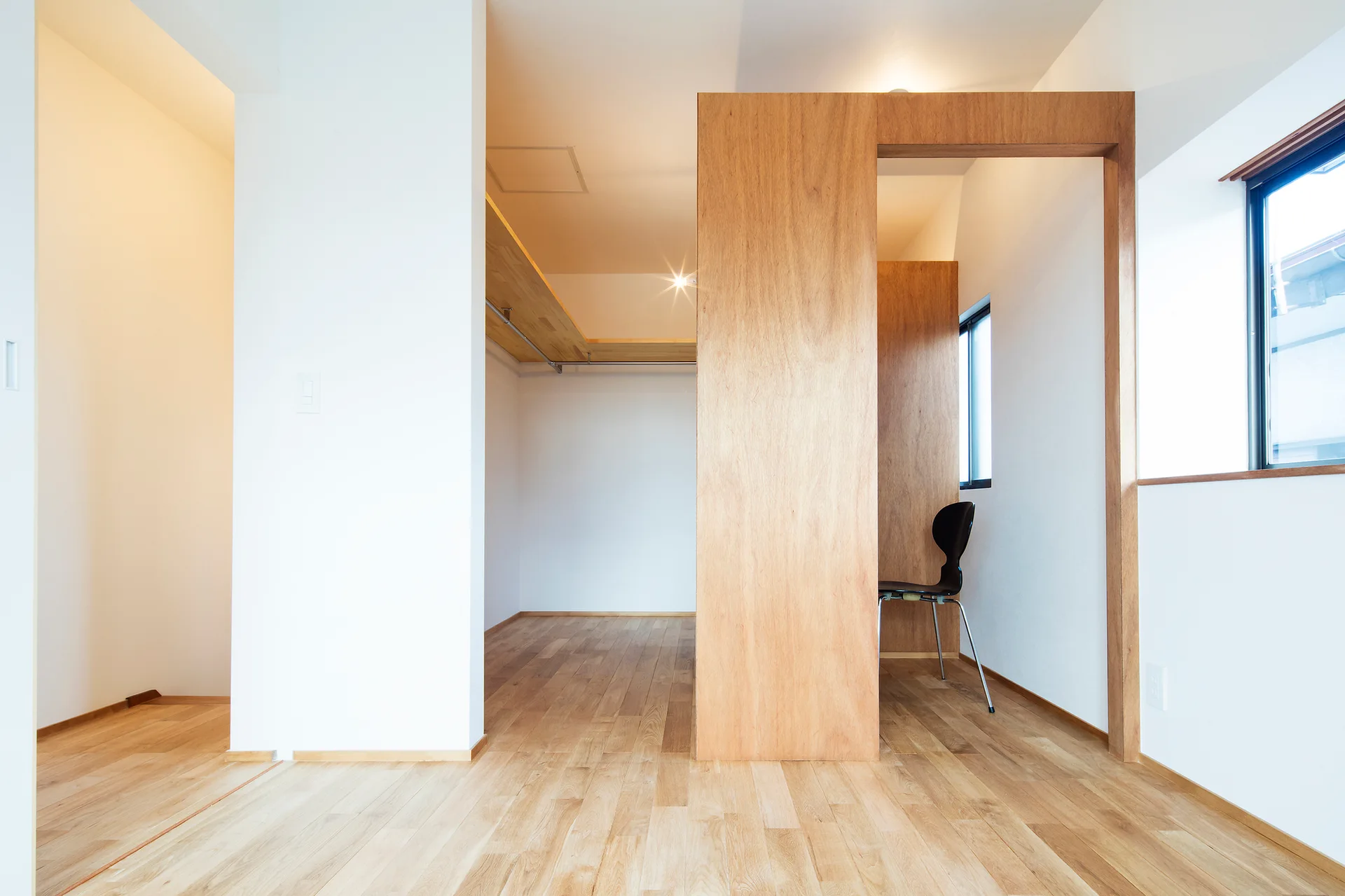 A minimalist dressing area featuring a light wood partition wall, hardwood floors, white walls, and open closet shelving.