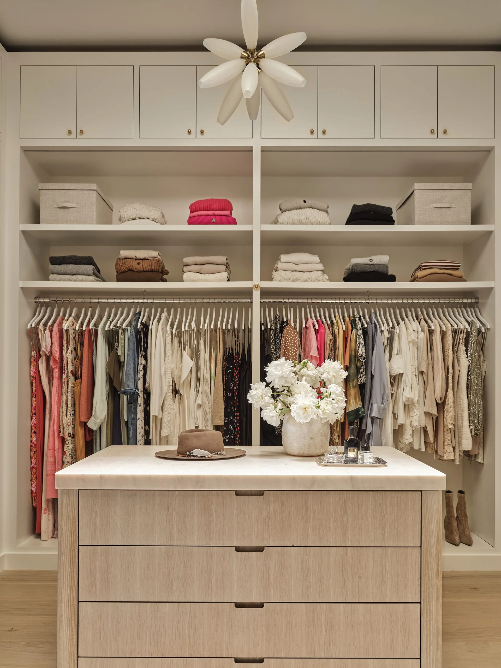 An organized walk-in closet featuring white built-in shelving, hanging clothes, and a light wood central island with a marble countertop.