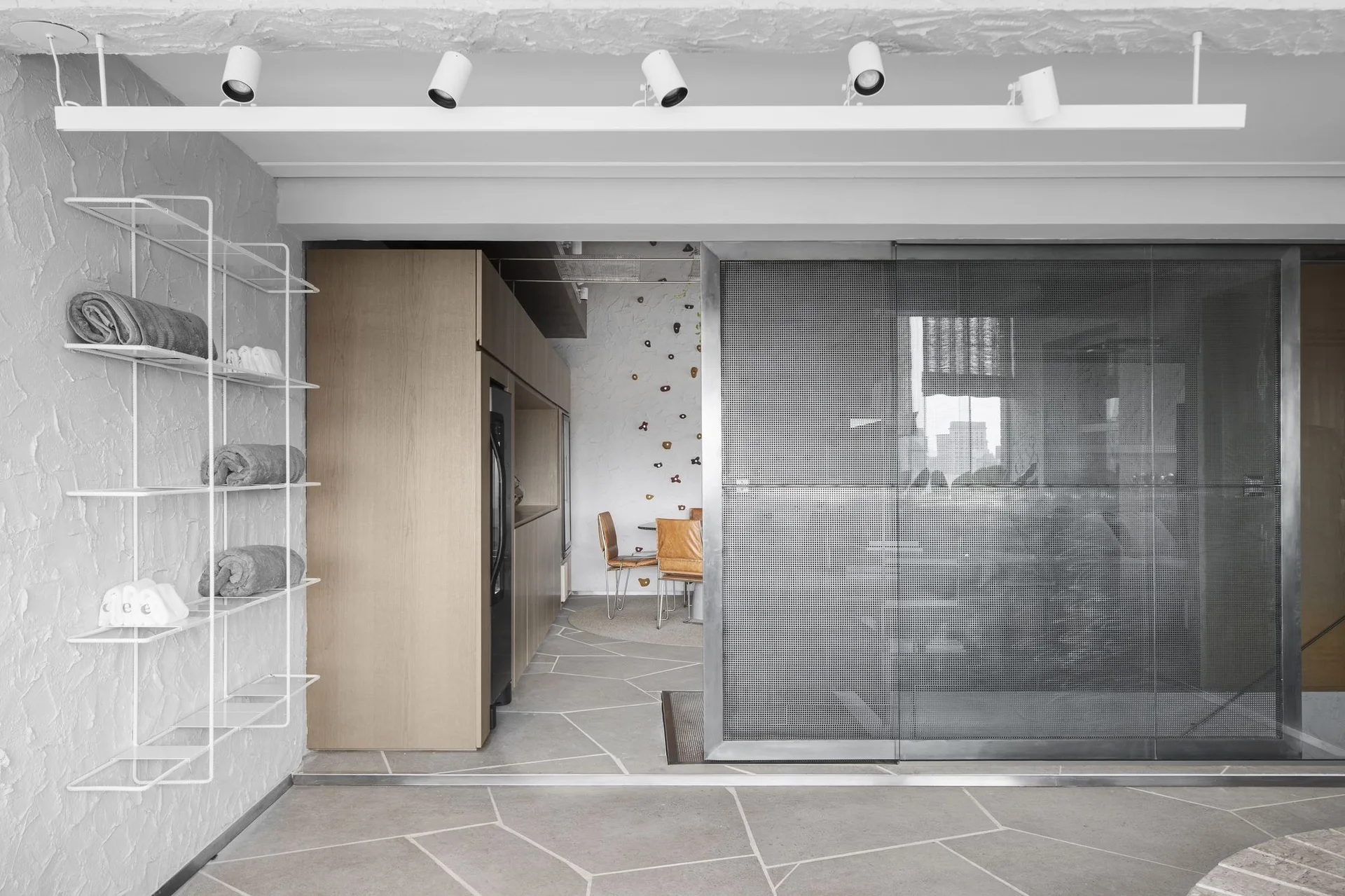 A modern interior space with grey stone floors, a textured white plaster wall, and a large sliding door made of perforated metal.