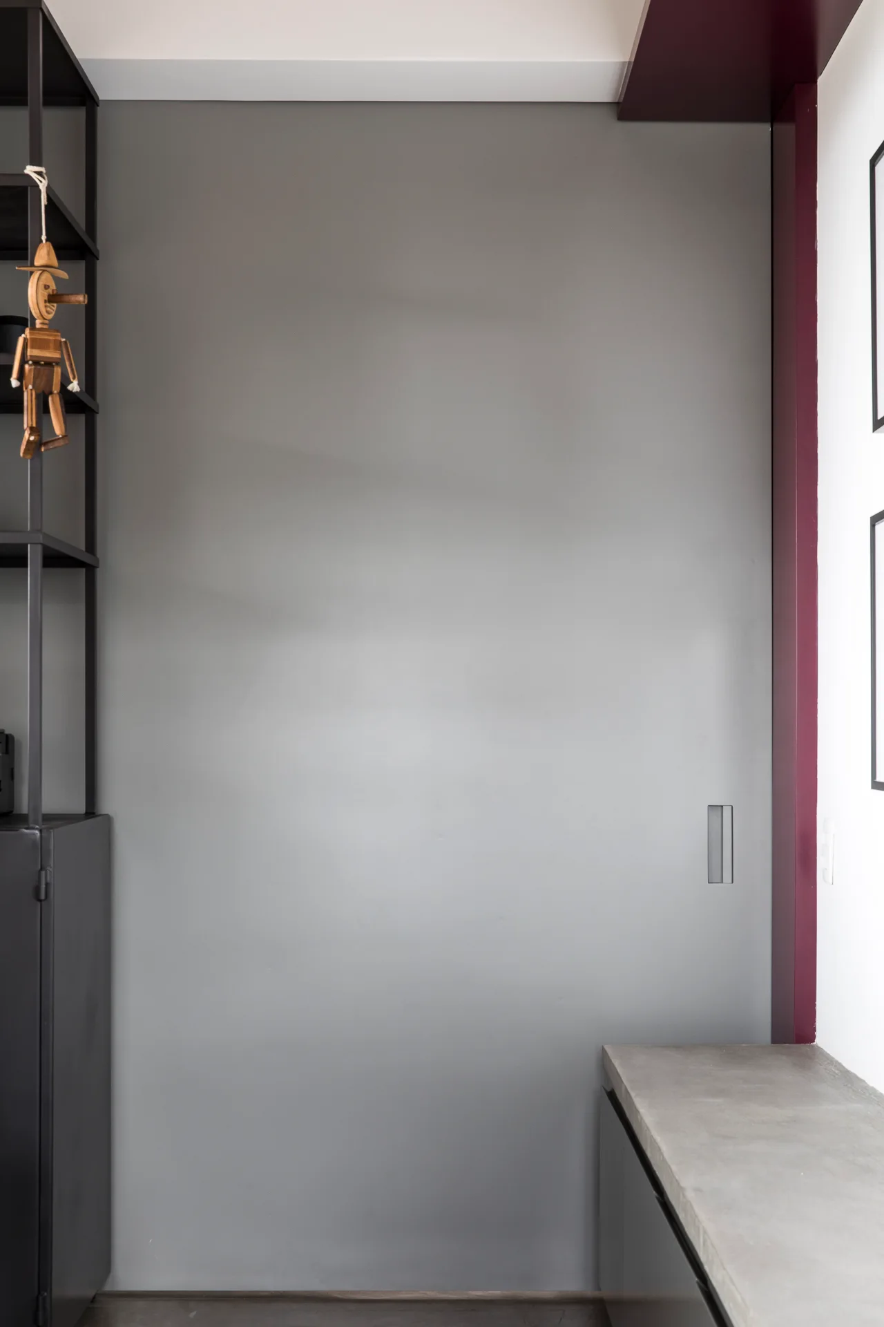 A matte grey sliding pocket door with a recessed handle is positioned next to a concrete-like countertop and a black metal shelving unit.
