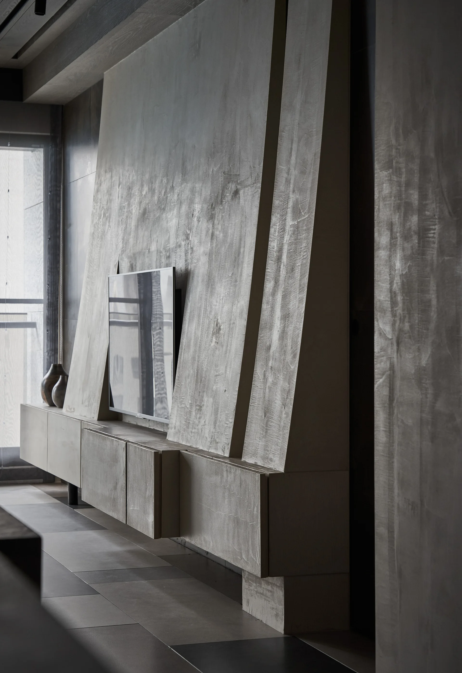 A textured greige plaster feature wall with an angled design stands behind a mounted flat-screen TV and a floating media cabinet.