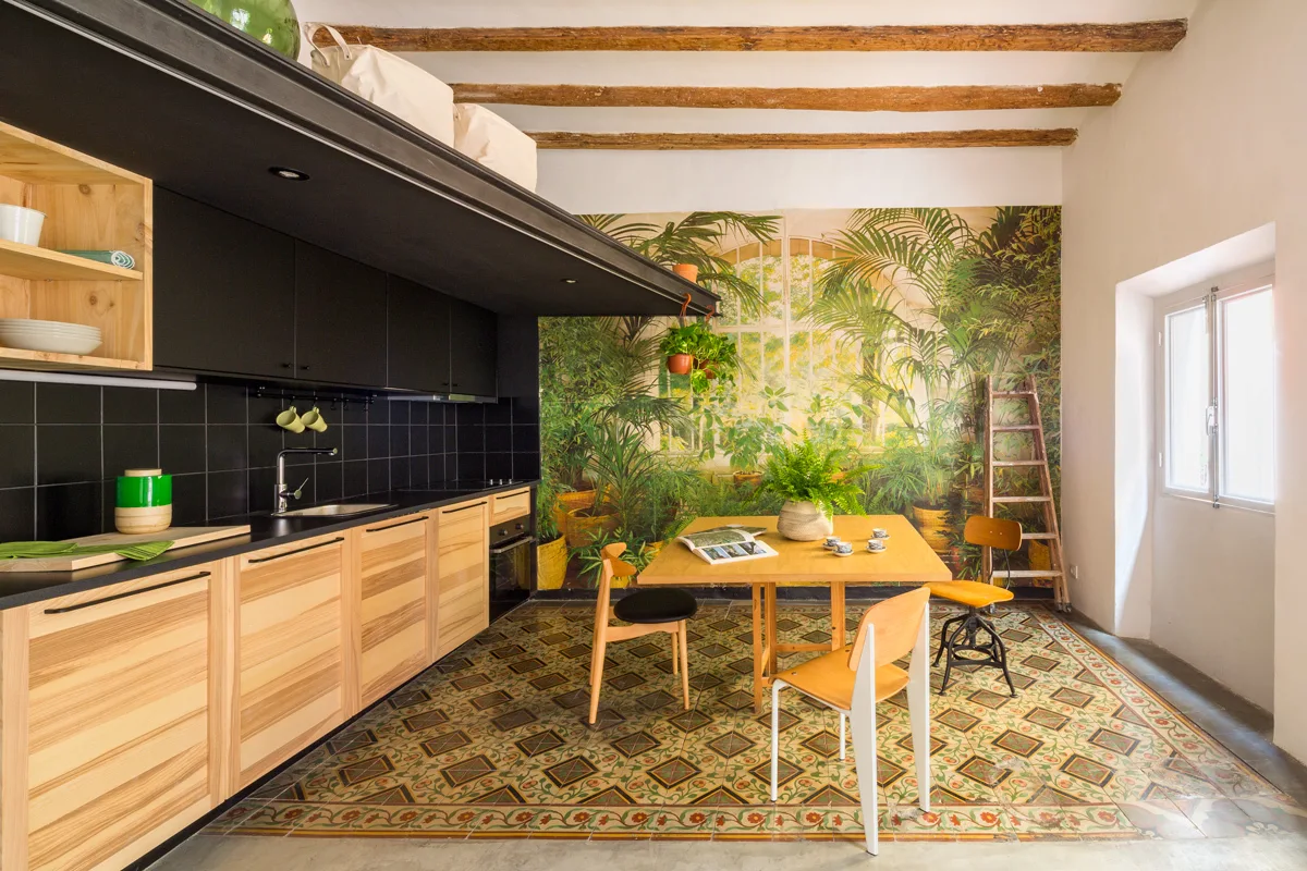 A rustic kitchen features wood lower cabinets, black upper cabinets, a large botanical wall mural, and green-patterned tile flooring.