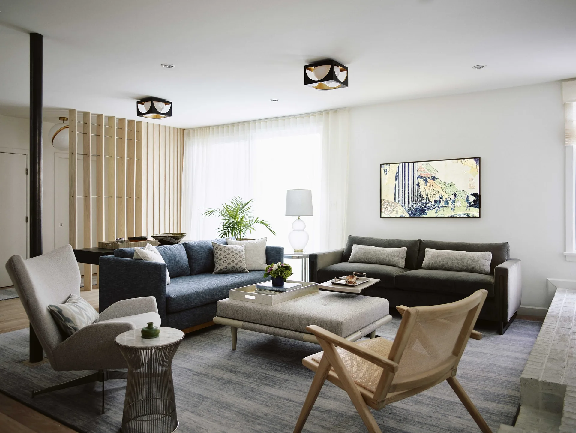 A contemporary living room featuring a blue sofa, a charcoal grey sofa, a slatted wood room divider, and a large grey textured rug.