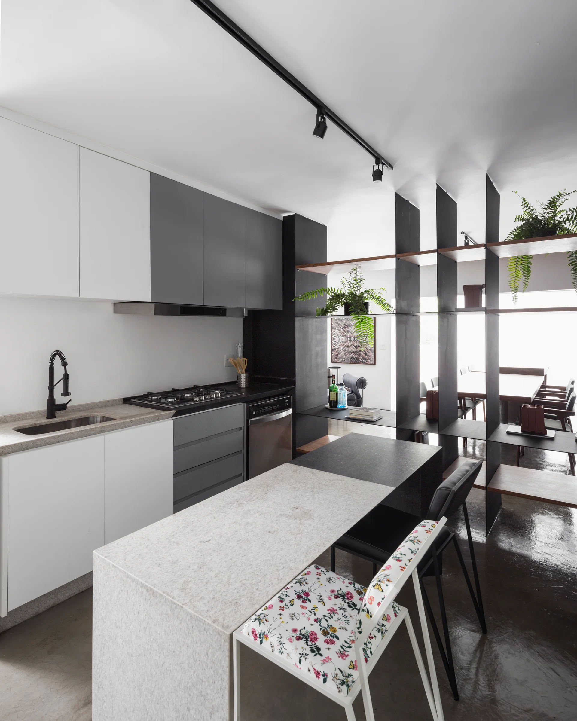A modern kitchen featuring two-tone cabinetry, a dual-surface stone island, and a tall black metal open-shelving room divider filled with green plants.