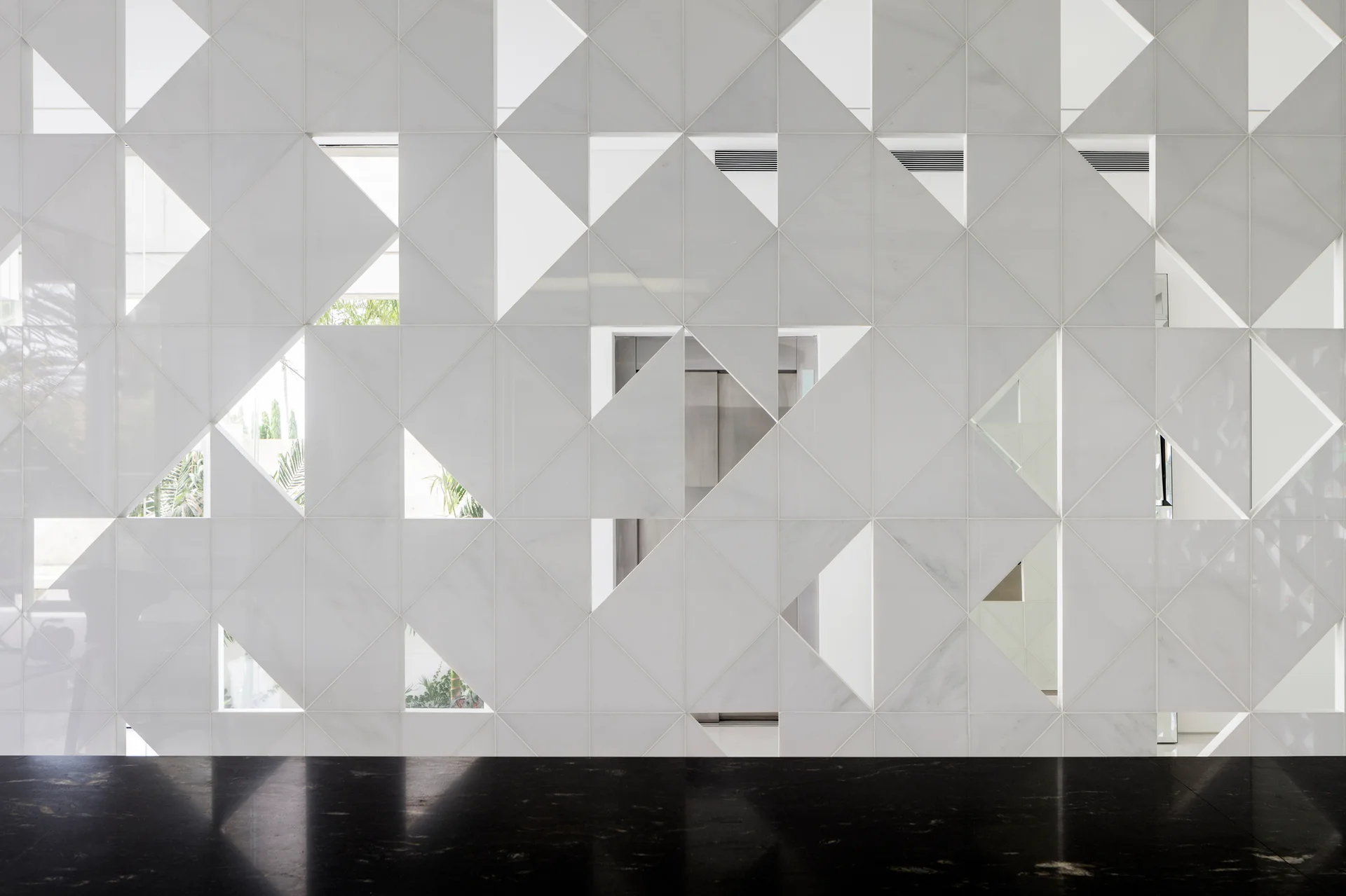 A modern white marble screen wall with triangular cutout patterns is paired with a highly polished black stone floor.