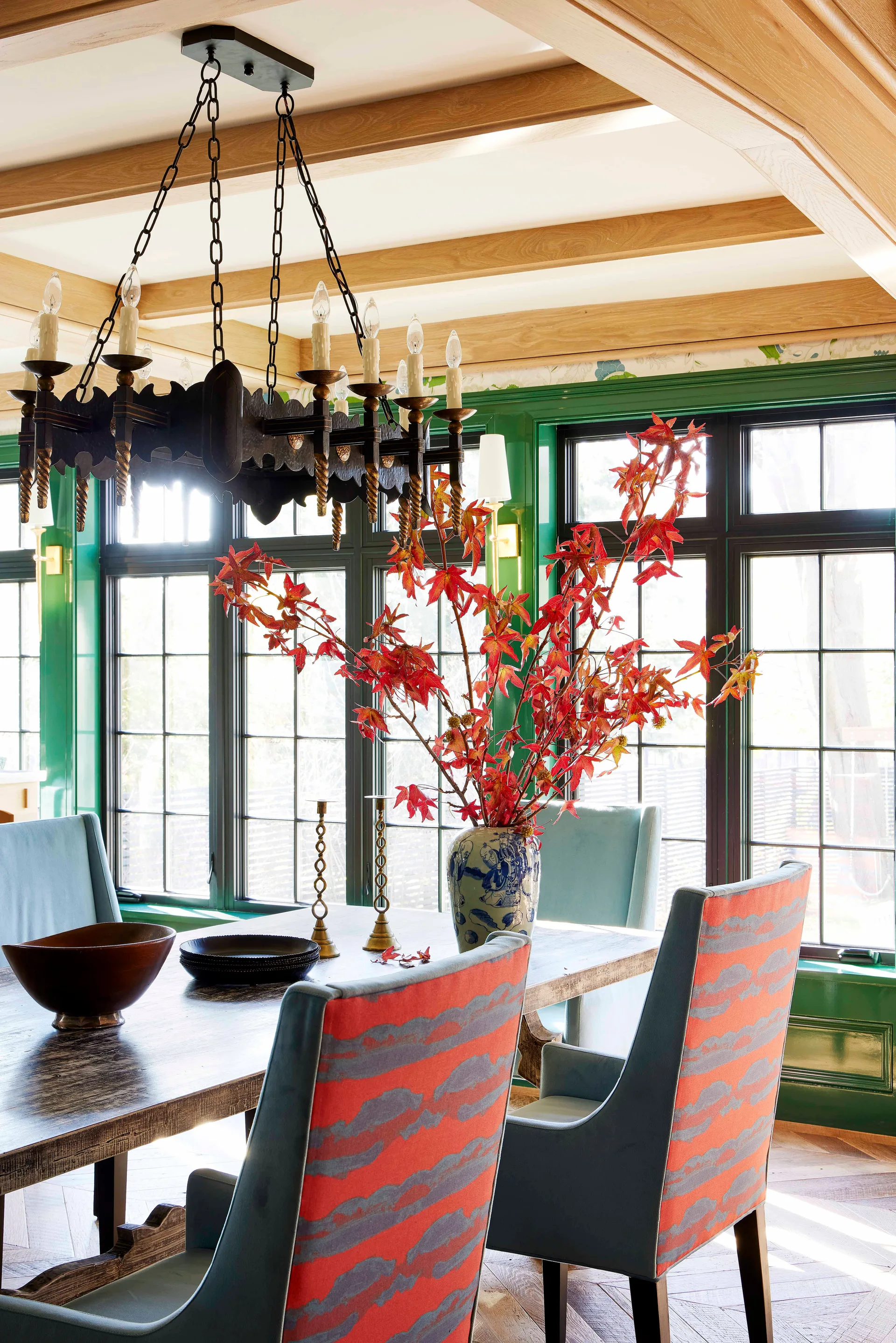 A dining room features glossy green paneled walls, a rustic wooden table with upholstered chairs, and wood ceiling beams.