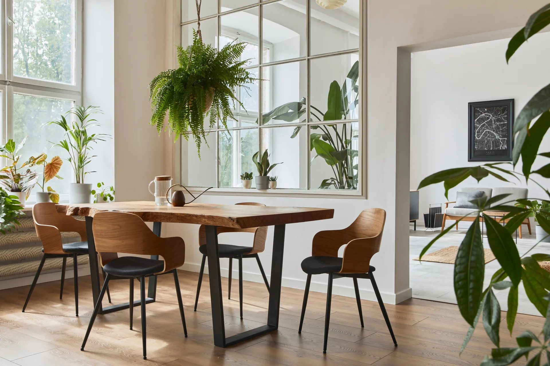 A bright dining room features a live-edge wooden table, curved wooden chairs with black cushions, and a large interior glass window with grid frames.