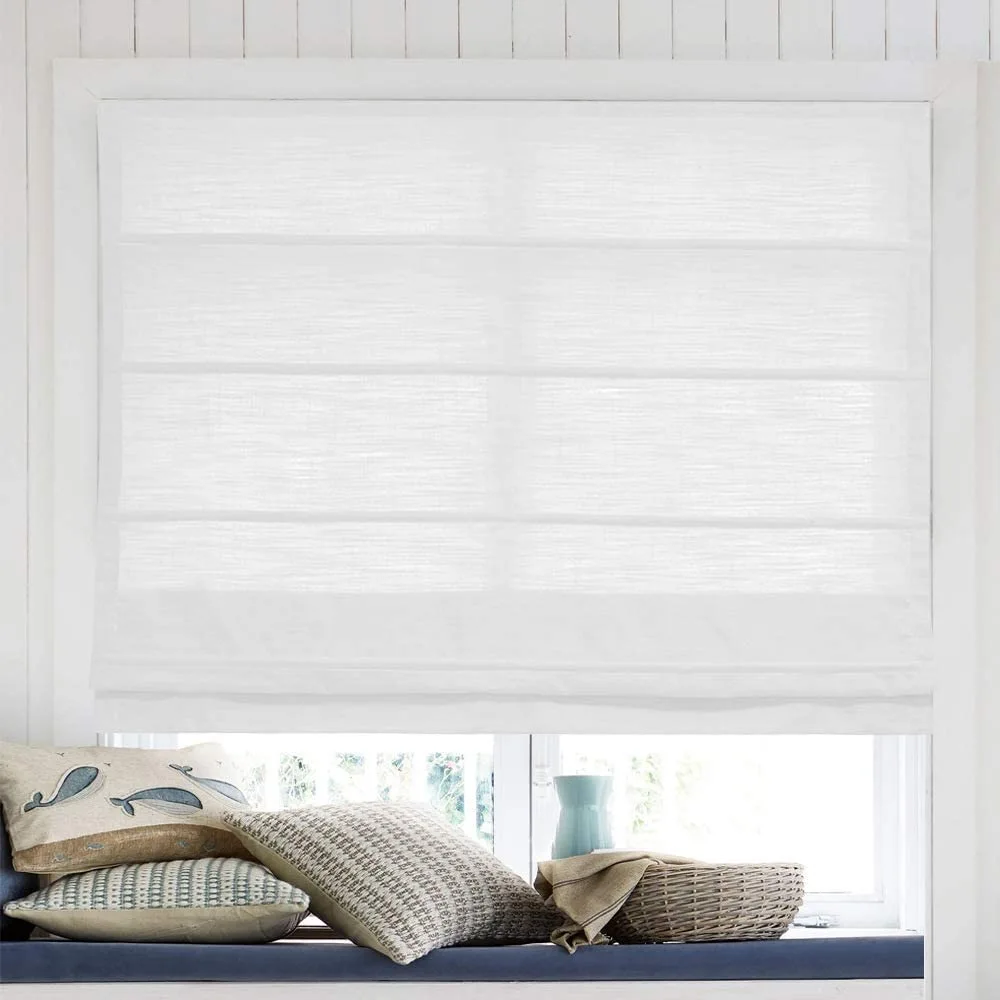 A white textured linen roman shade covers a window above a blue cushioned bench with coastal throw pillows and a wicker basket.
