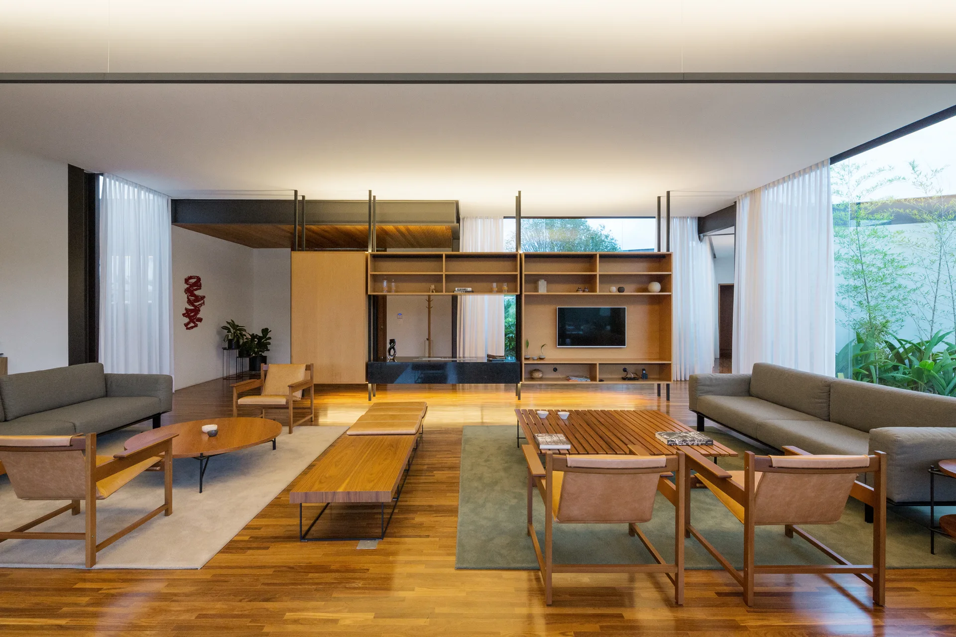 A large open living room features two distinct seating areas with grey sofas, leather armchairs, and a custom wooden room divider partition.