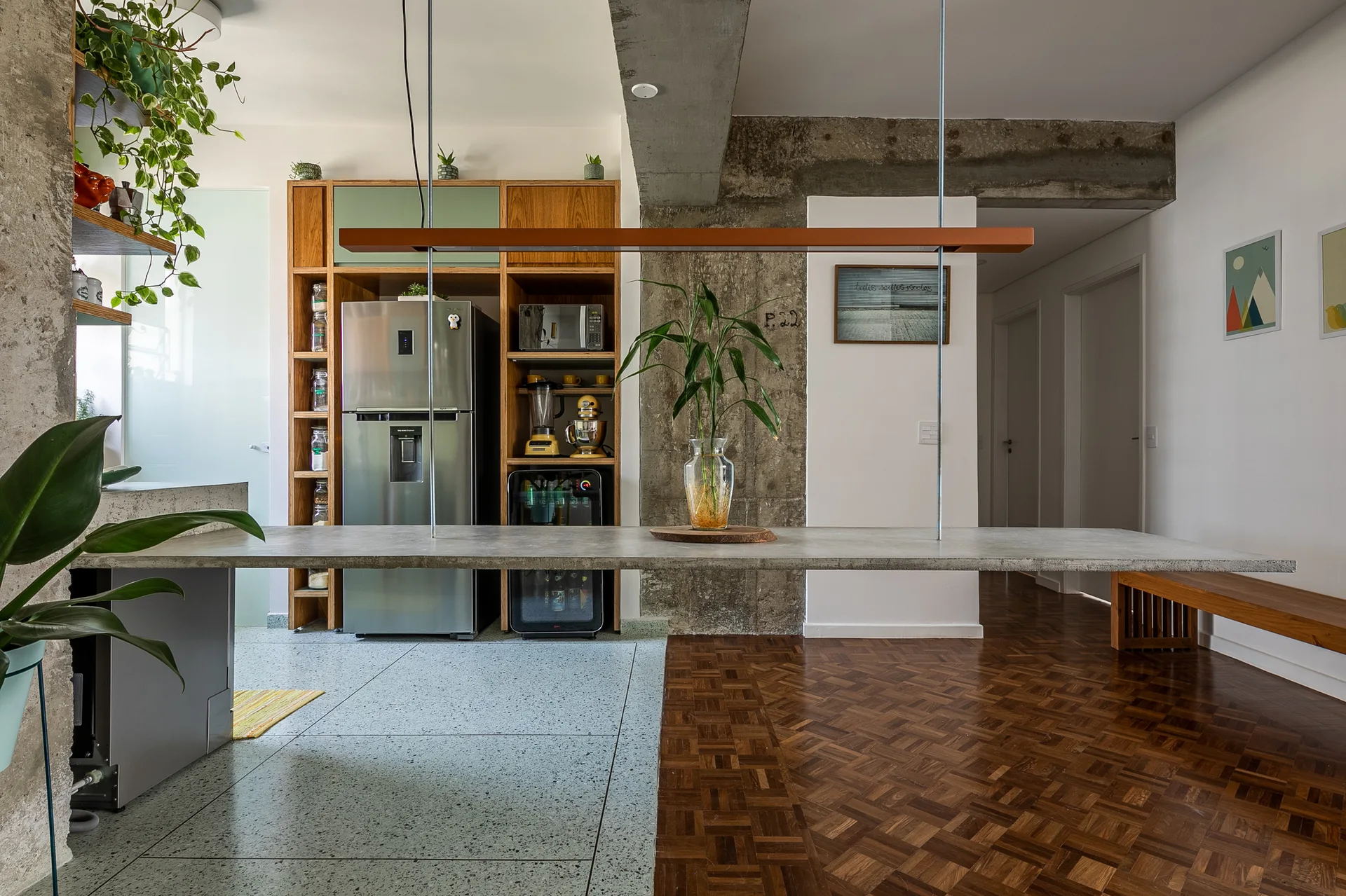 An industrial modern kitchen features a suspended concrete countertop, a built-in wood pantry cabinet, and a transition from tile to parquet flooring.