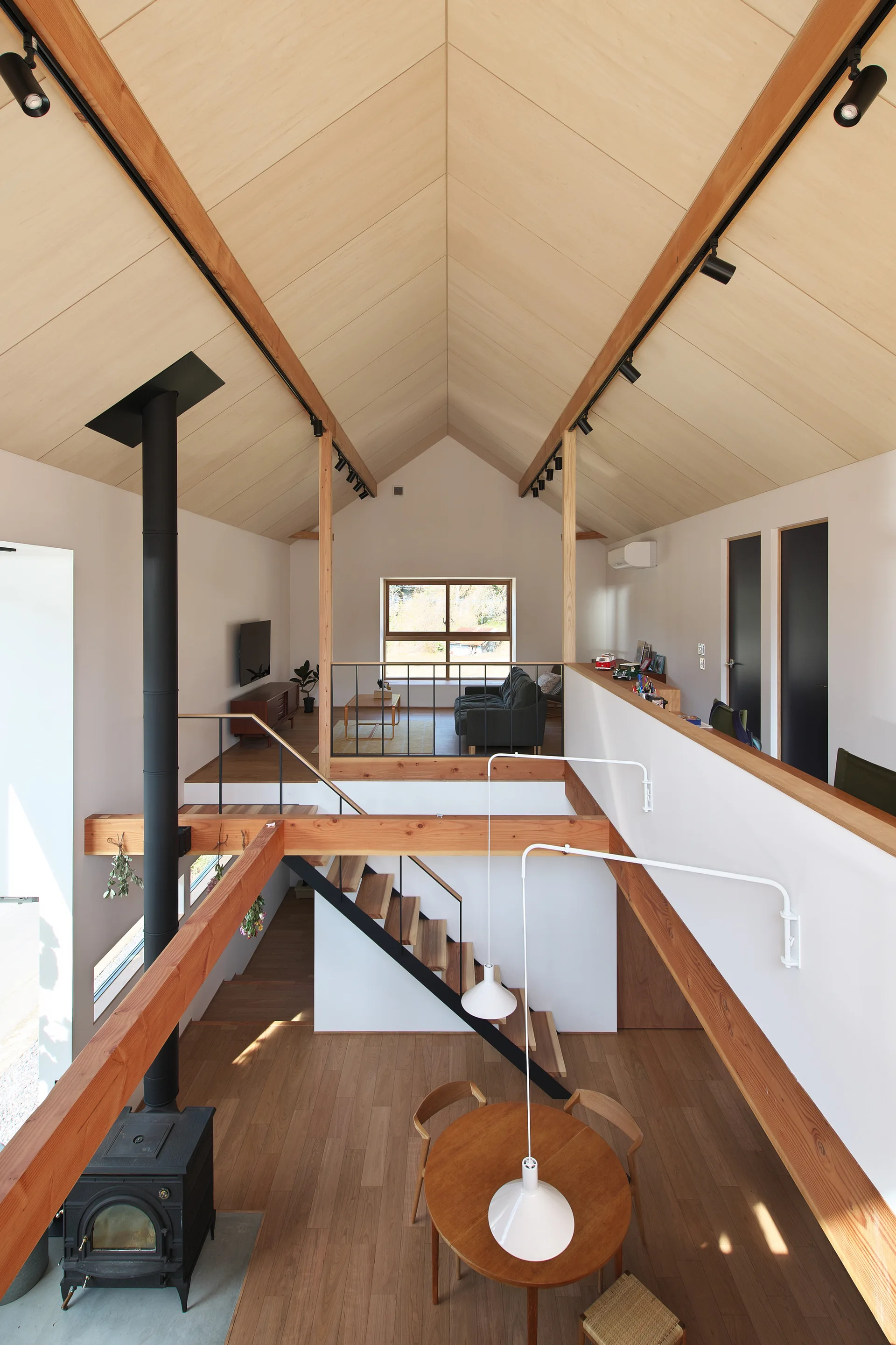 High-angle view of a multi-level home interior with a vaulted wood ceiling, mezzanine living area, and a dining room with a round wooden table.