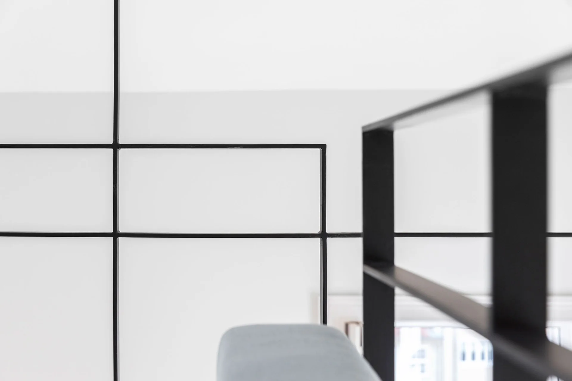 A close-up of a minimalist black steel staircase railing with a geometric grid design set against a plain white wall.