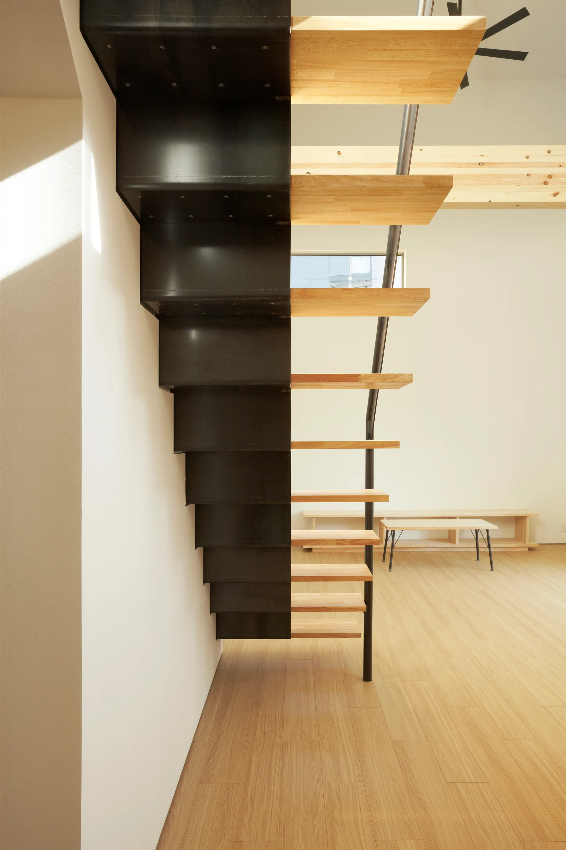Minimalist floating staircase with natural wood treads and black metal risers set against a white wall and light wood floors.