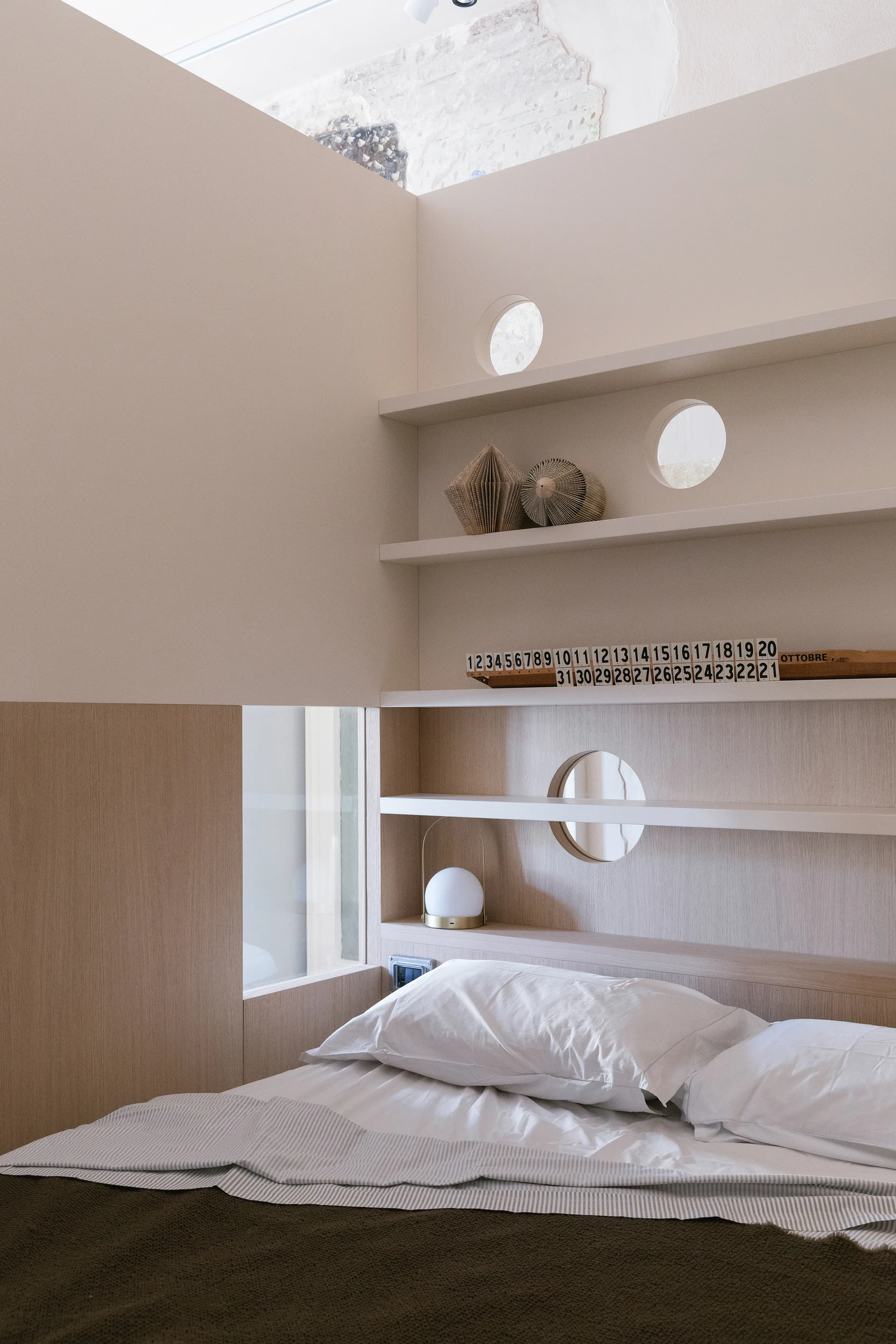 A minimalist bedroom featuring a bed with white pillows and a light wood built-in shelving unit with decorative circular cutouts.