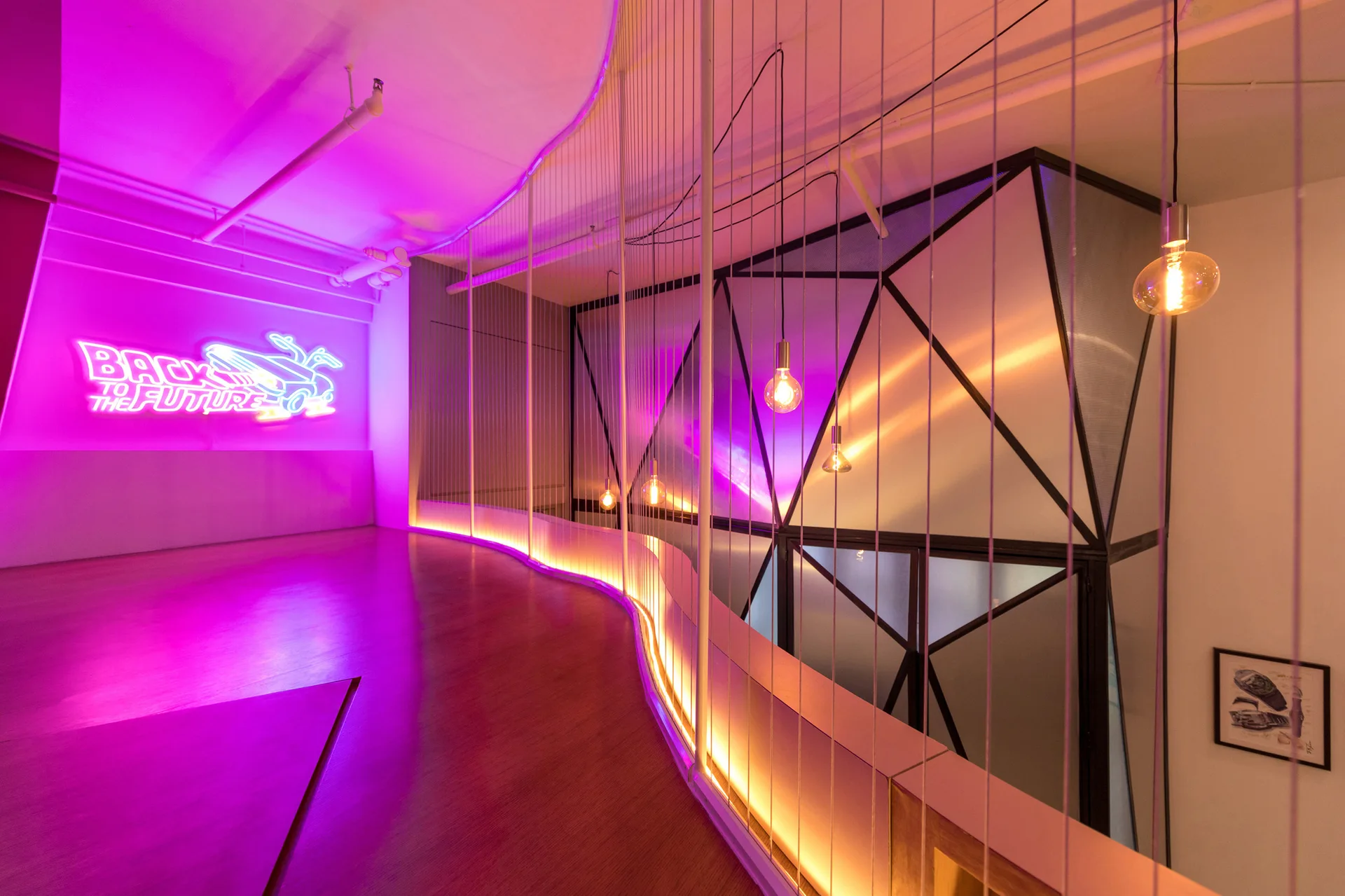 A modern hallway features a curved wooden floor, a black geometric screen, hanging bulb pendants, and a glowing purple neon sign.