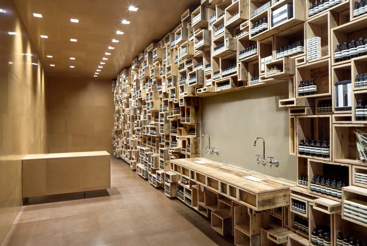 A commercial interior features a floor-to-ceiling wall of stacked wooden crate shelves alongside a matching wood counter with chrome faucets.
