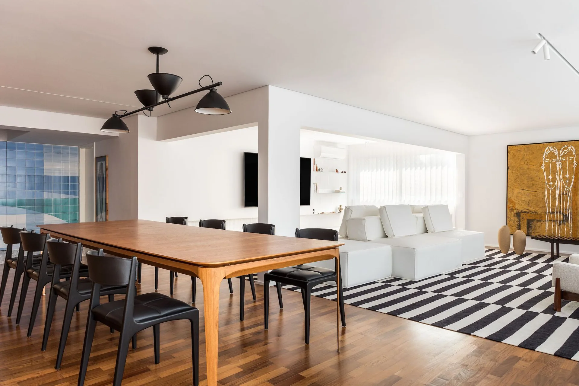 An open-plan living and dining area features a wood dining table, black chairs, a modular white sofa, and a bold black and white striped rug.
