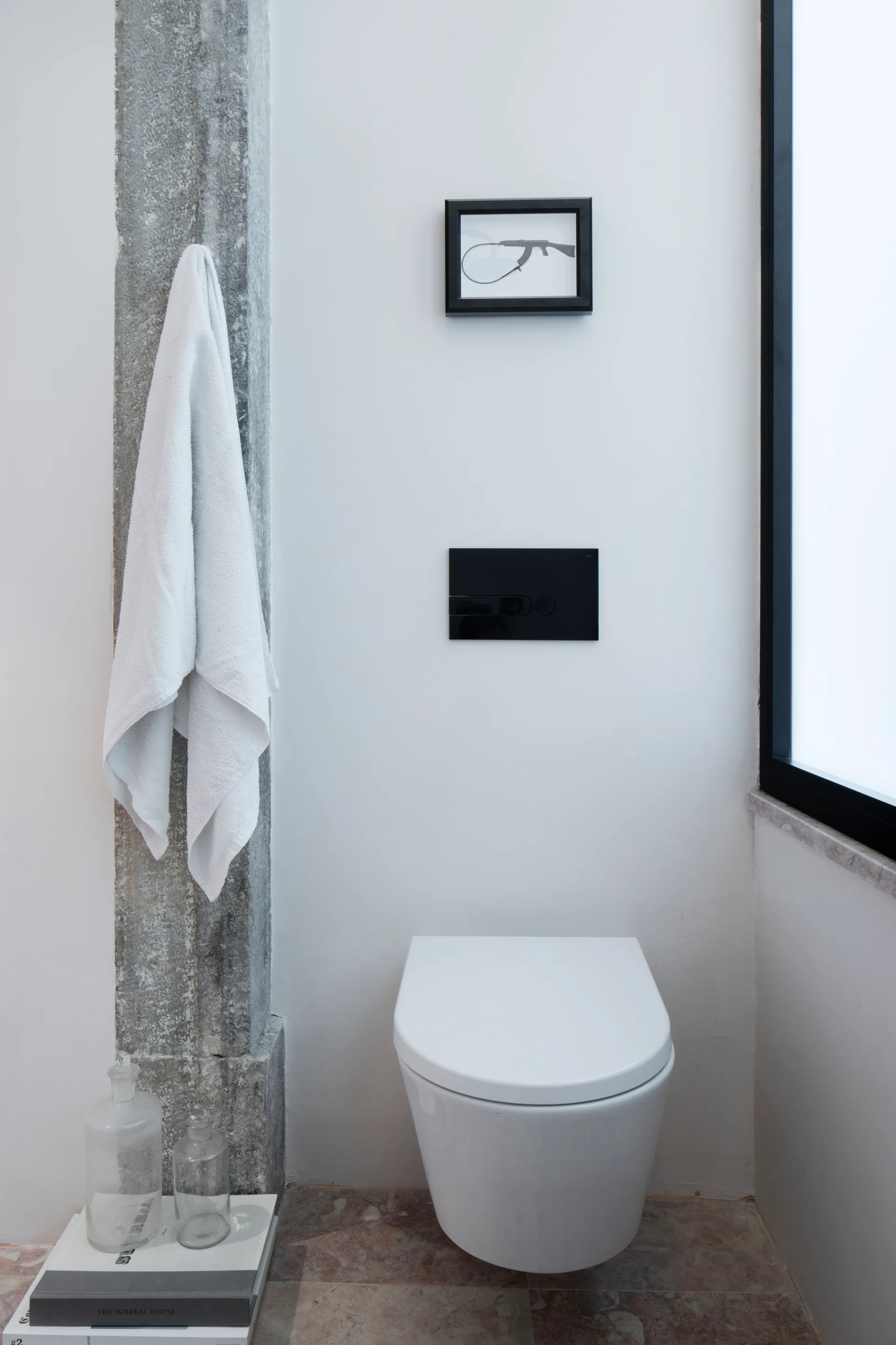 A wall-mounted white toilet on a mottled stone floor next to a rough grey stone column with a hanging white towel.