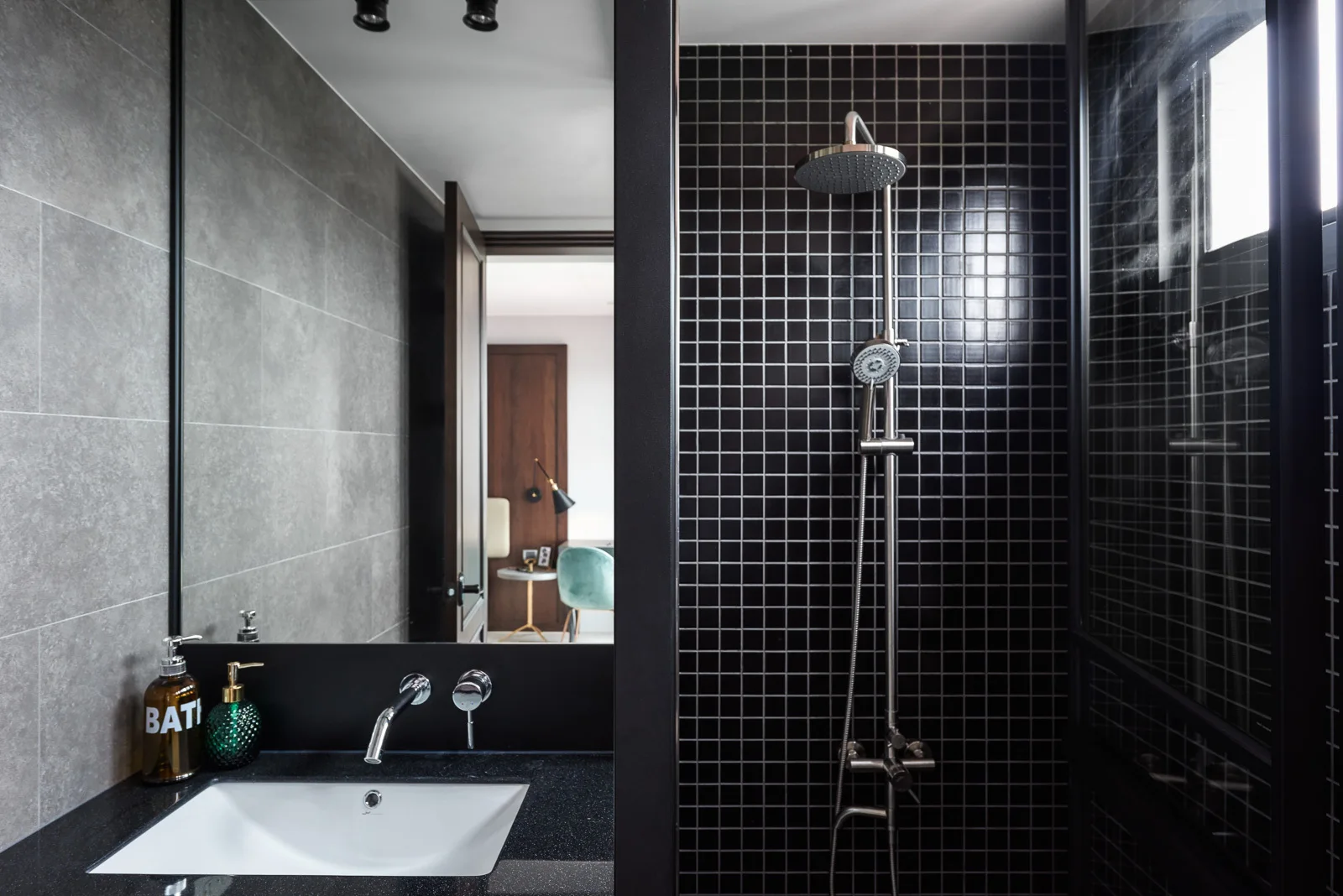 A modern bathroom featuring a black grid-tiled shower, chrome fixtures, a dark vanity countertop with an under-mount sink, and a large mirror.
