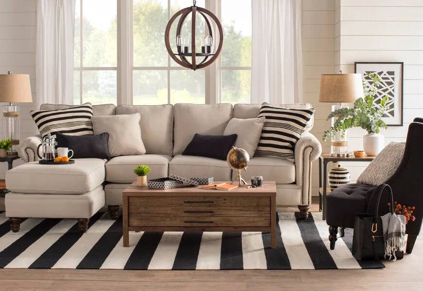 A cream sectional sofa sits on a bold black and white striped rug in a bright room with white shiplap walls.