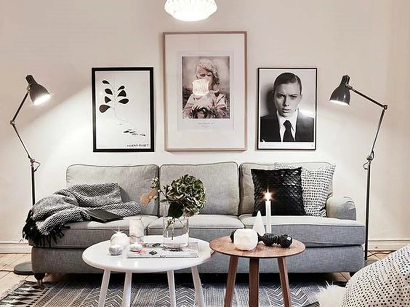 A light grey sofa is flanked by two black metal floor lamps under three framed black and white art prints on a wall.