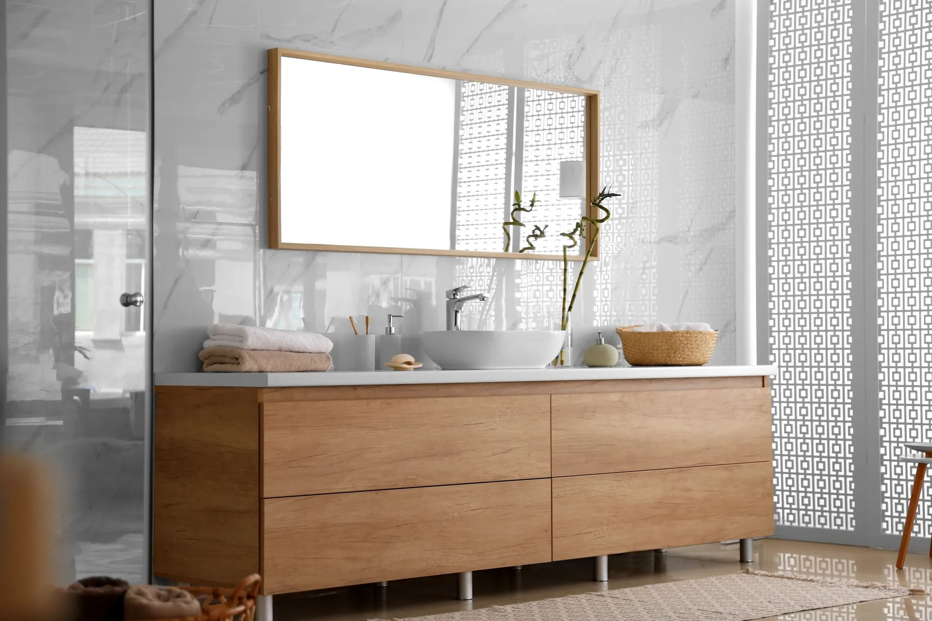 A modern bathroom features a wood vanity with a white vessel sink, a matching framed mirror, and glossy marble-look tiled walls.
