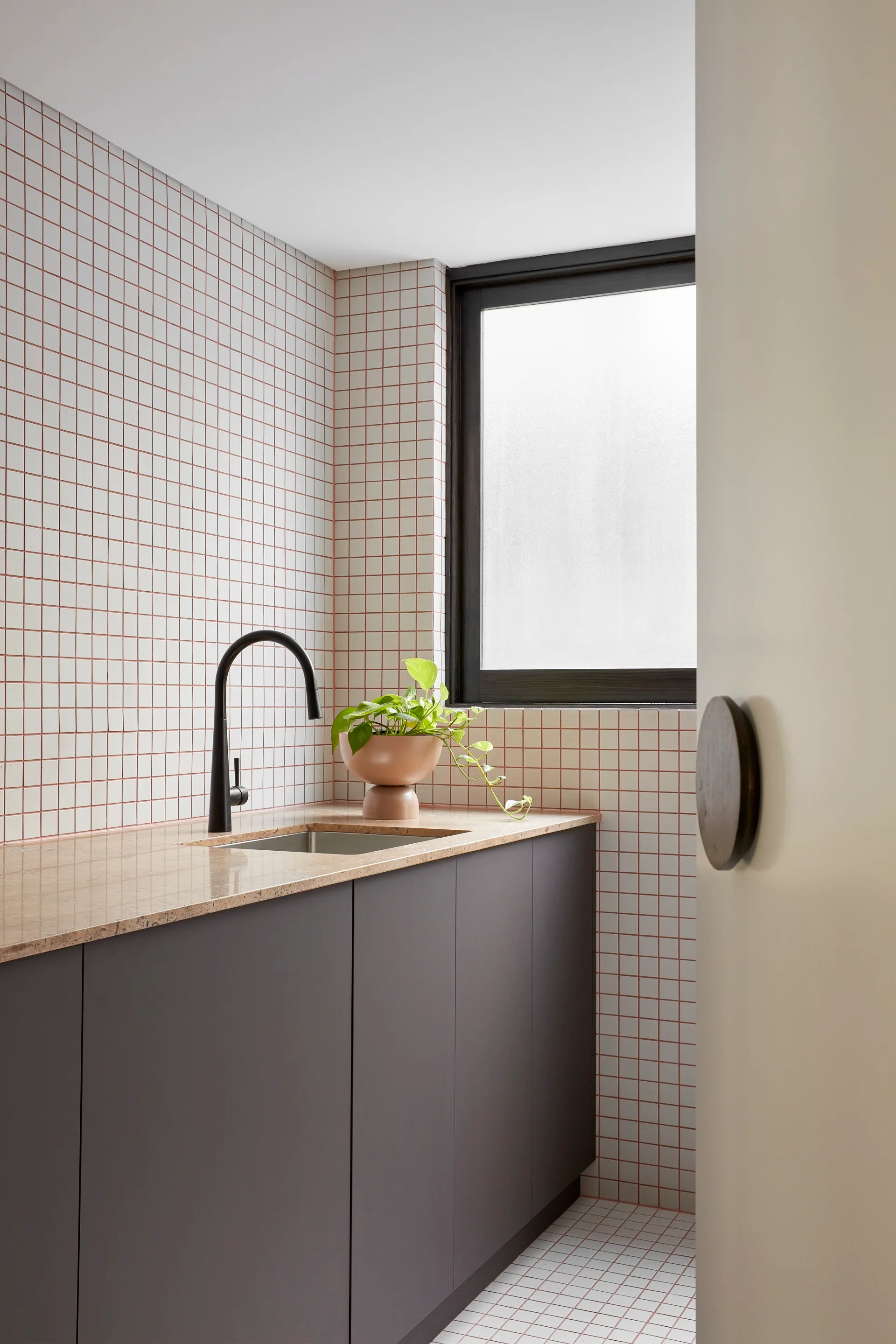 A modern bathroom vanity with dark grey cabinets, a speckled countertop, an arched black faucet, and white square tiled walls with red grout.