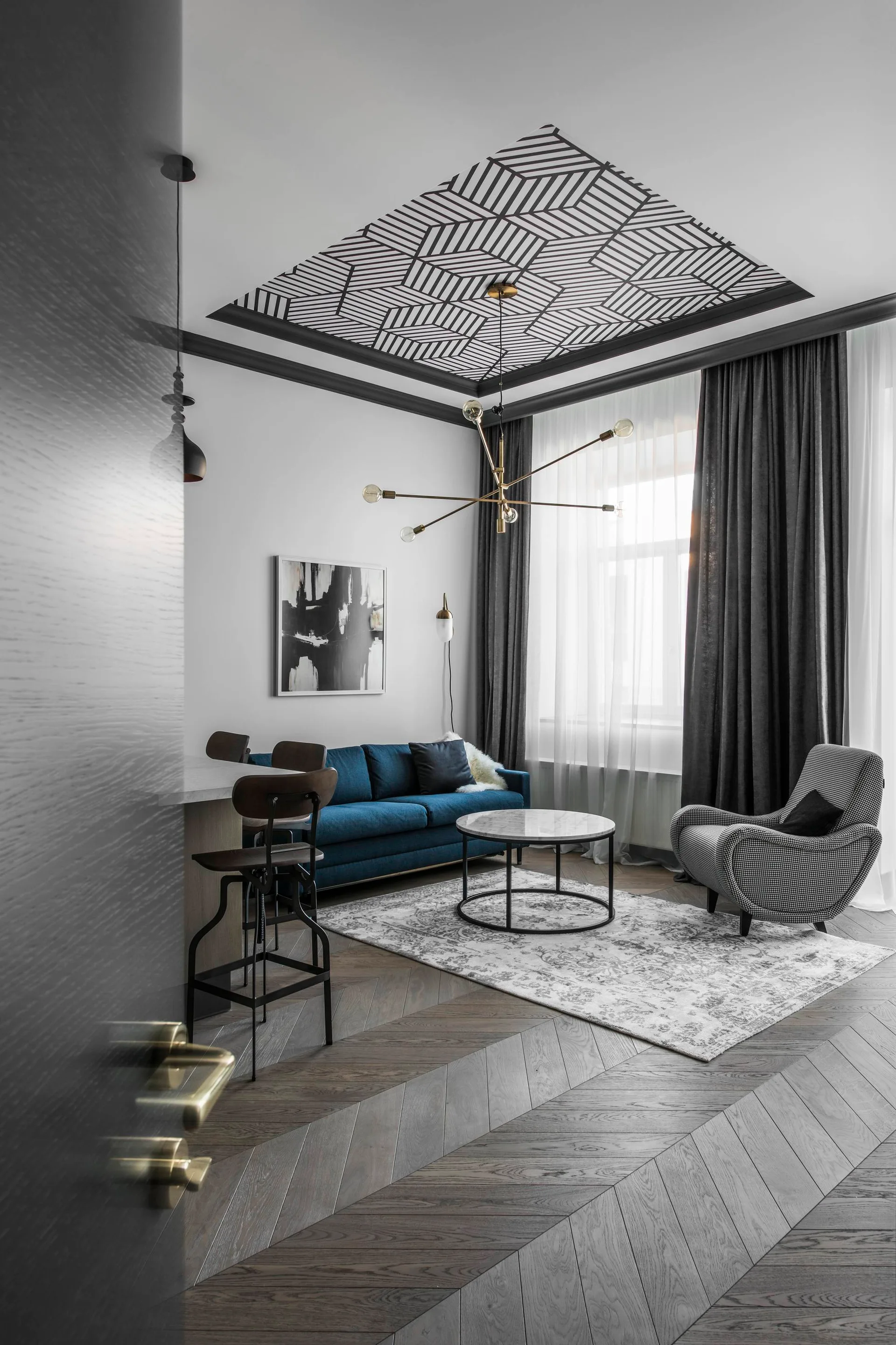 A modern living room features a blue sofa, a houndstooth armchair, a round marble coffee table, and a black and white geometric ceiling pattern.