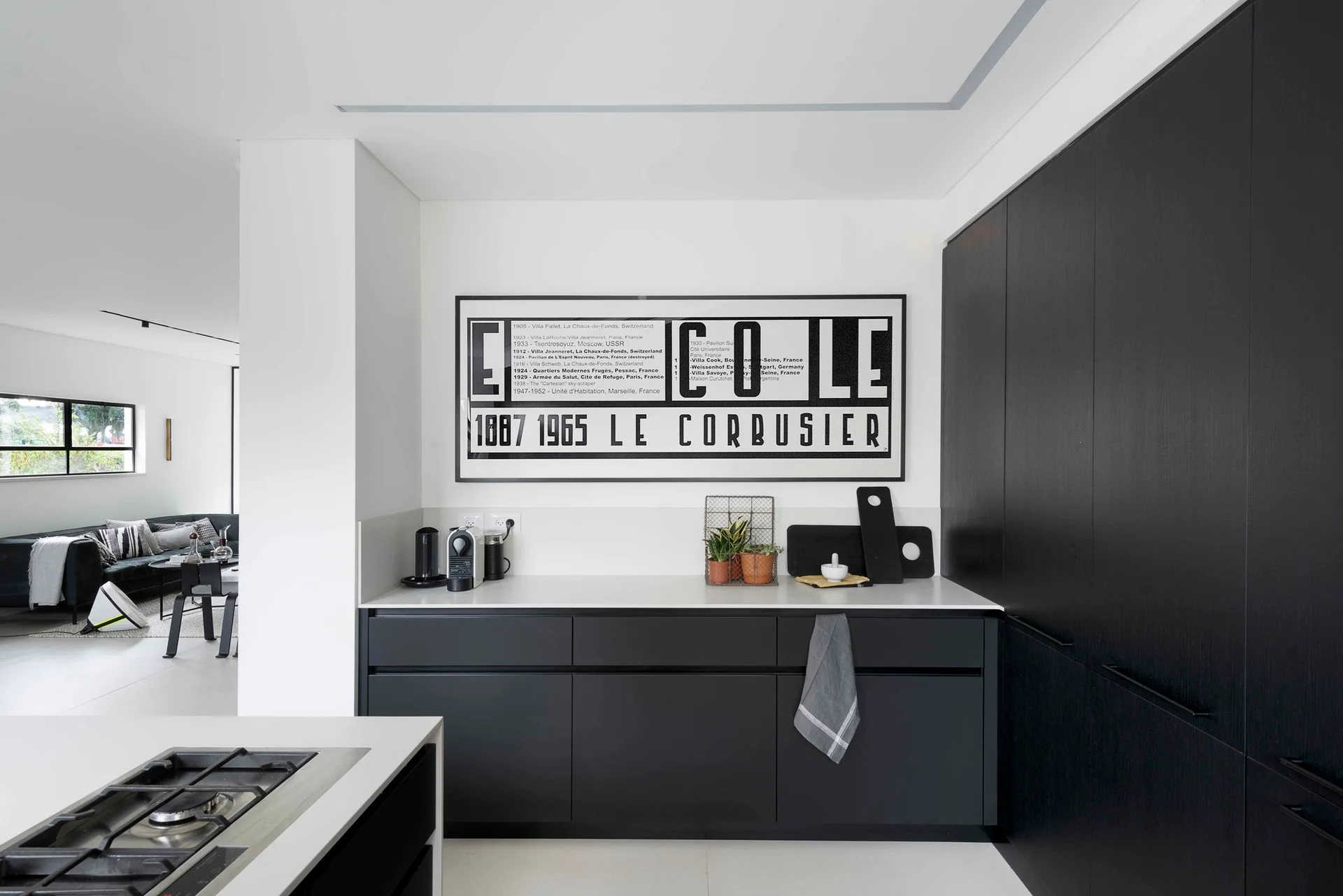 A minimalist modern kitchen features matte black cabinetry, white countertops, and a large framed black-and-white print of graphic text on the wall.