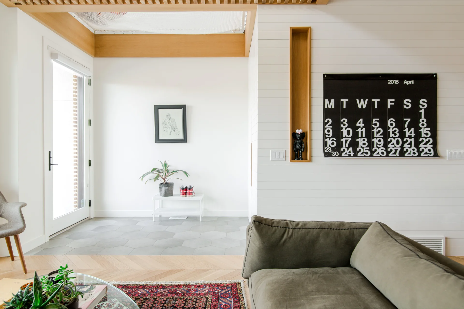 An entryway featuring gray hexagonal floor tiles, white shiplap walls with a recessed wood niche, and an olive green sofa in the foreground.
