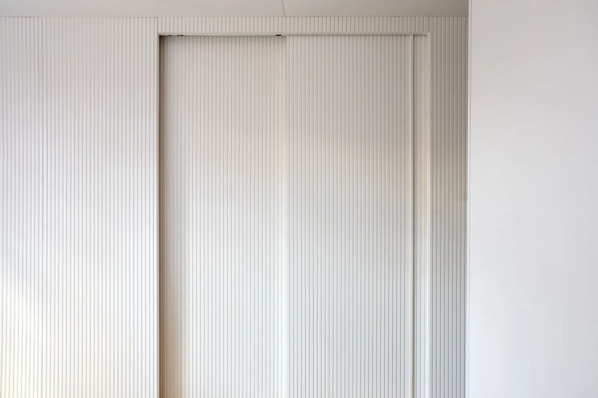 Close-up of matte white fluted wall paneling with an integrated sliding door showing clean vertical ribbing.