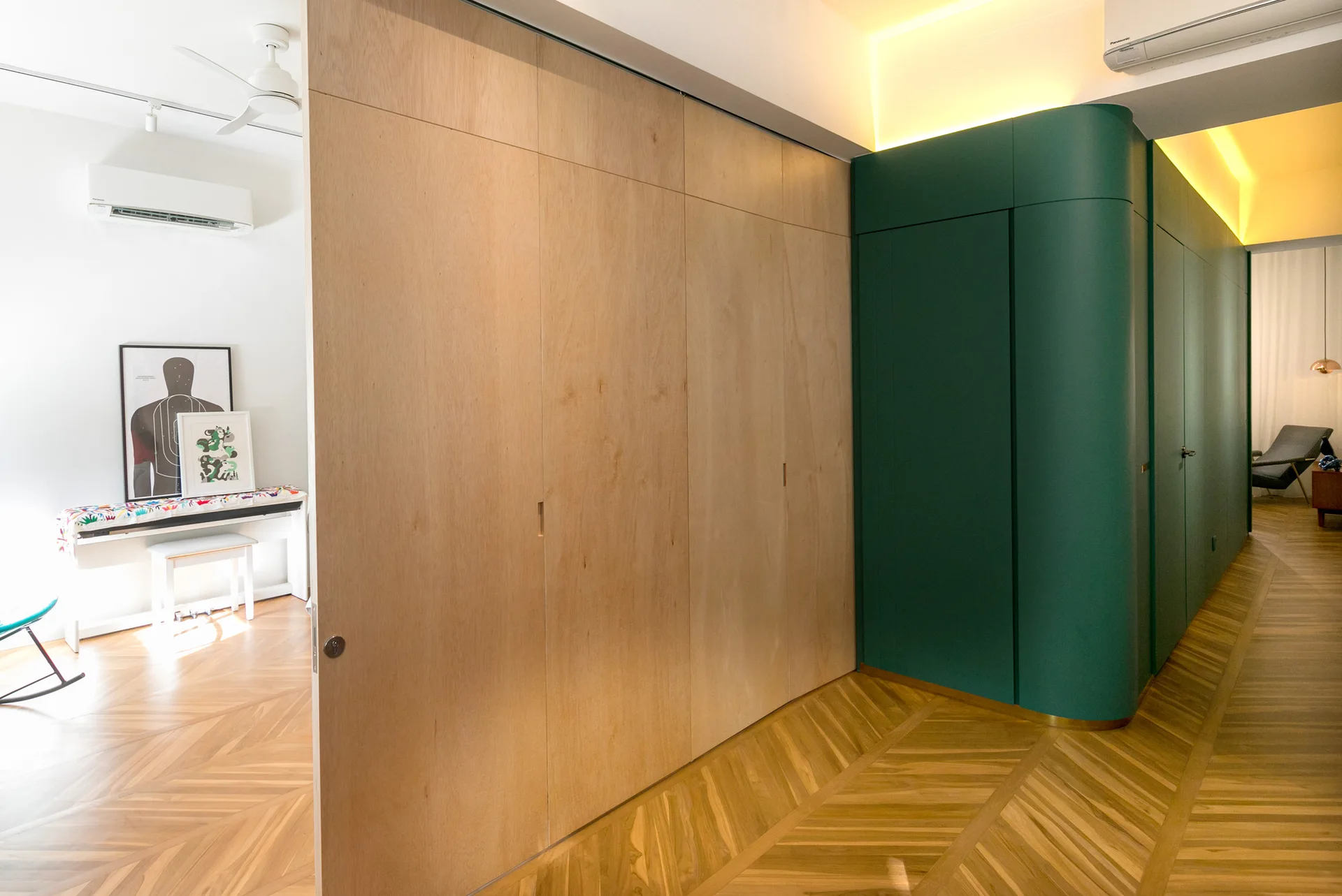 A modern hallway features a curved forest green partition wall next to a seamless light wood storage wall and chevron patterned wood flooring.