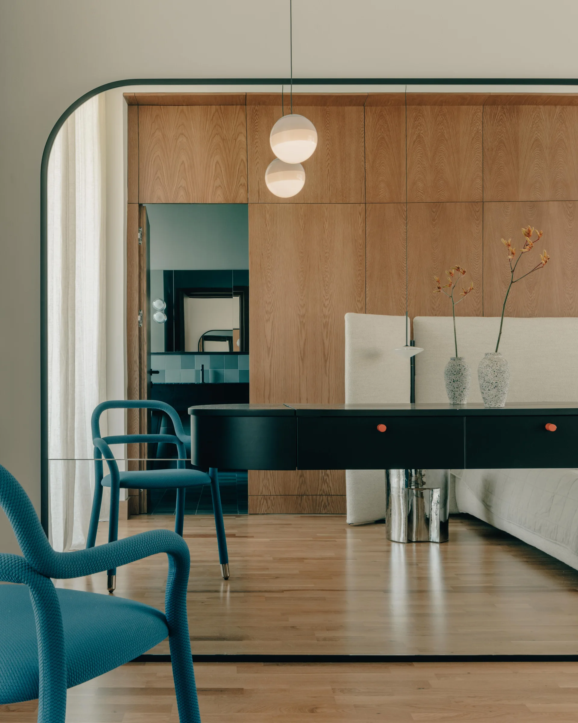 A modern interior framed by a black archway features bright blue sculptural chairs, a black console desk, and natural wood wall paneling.