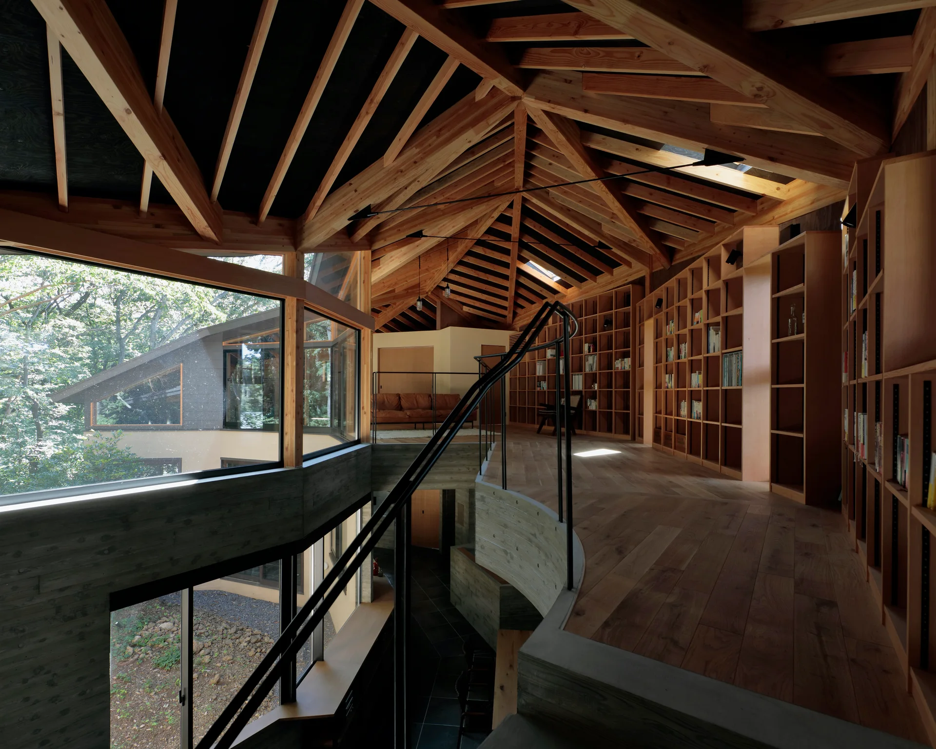 A split-level home interior featuring a wood-paneled library mezzanine with curved concrete walkways, built-in wooden shelving, and exposed timber rafters.