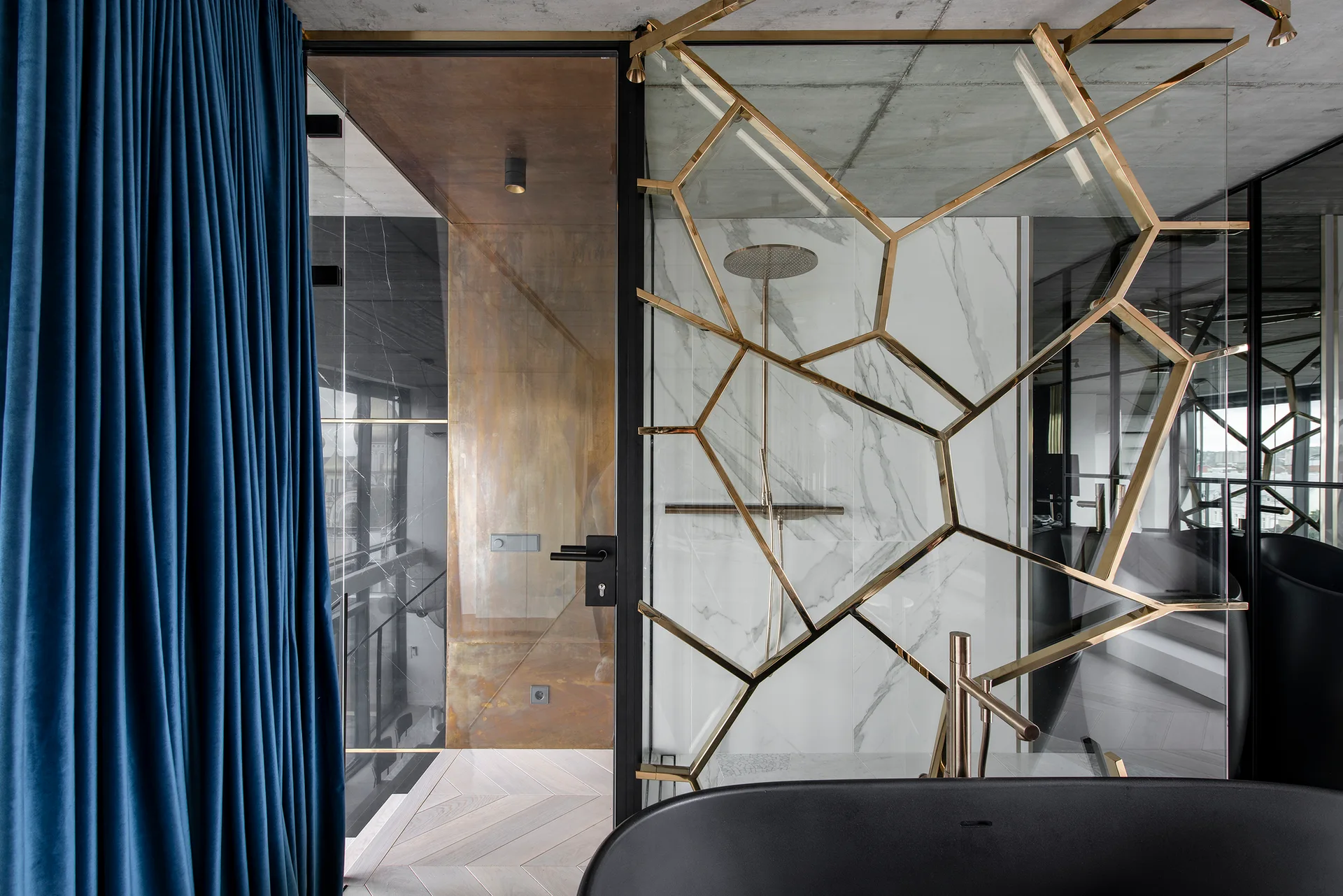 A modern bathroom features a gold geometric glass shower screen, white marbled walls, a matte black bathtub, and a dark blue velvet curtain.