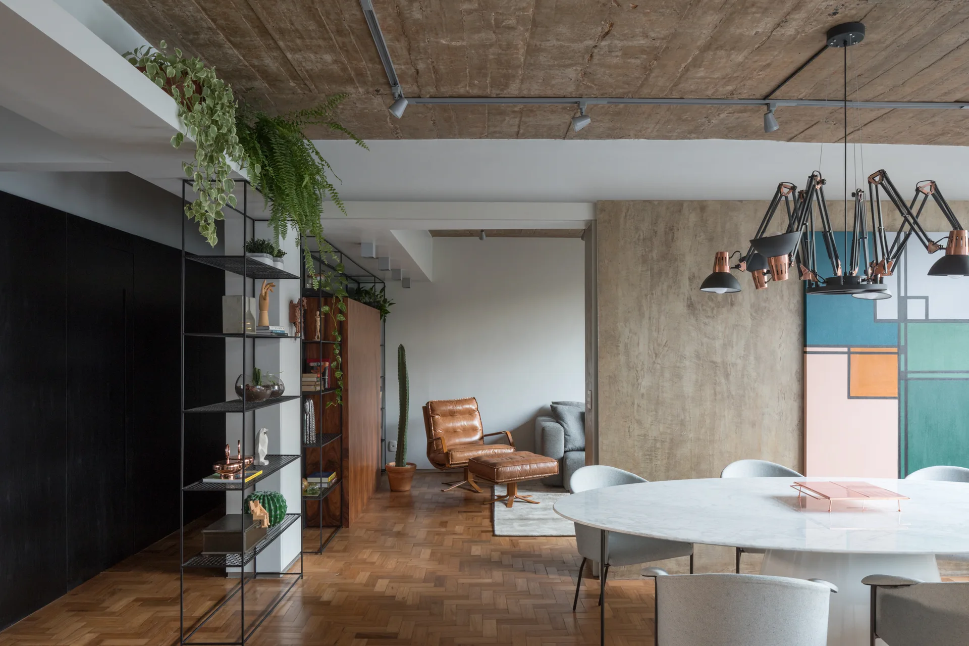 A modern dining room features a round marble table, grey chairs, an industrial chandelier, and an exposed concrete ceiling above parquet floors.