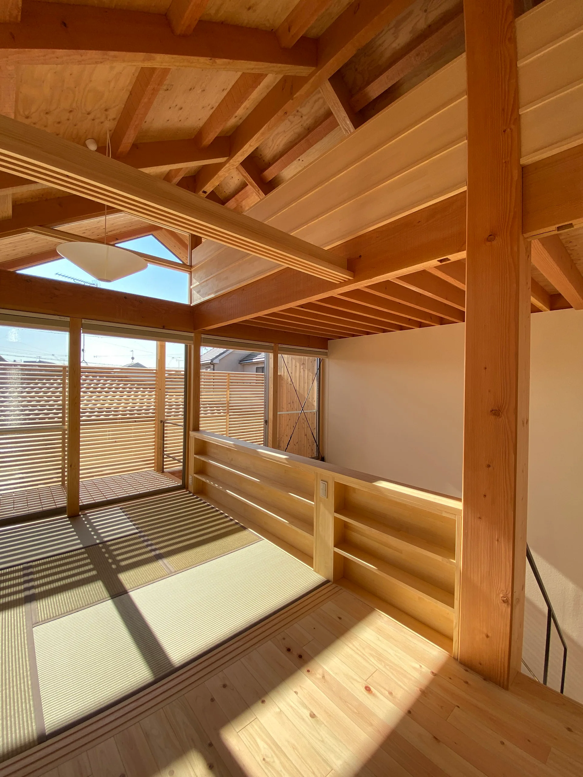 A modern wood-framed loft landing features a recessed tatami mat floor section, exposed timber rafters, and built-in low wooden shelving.