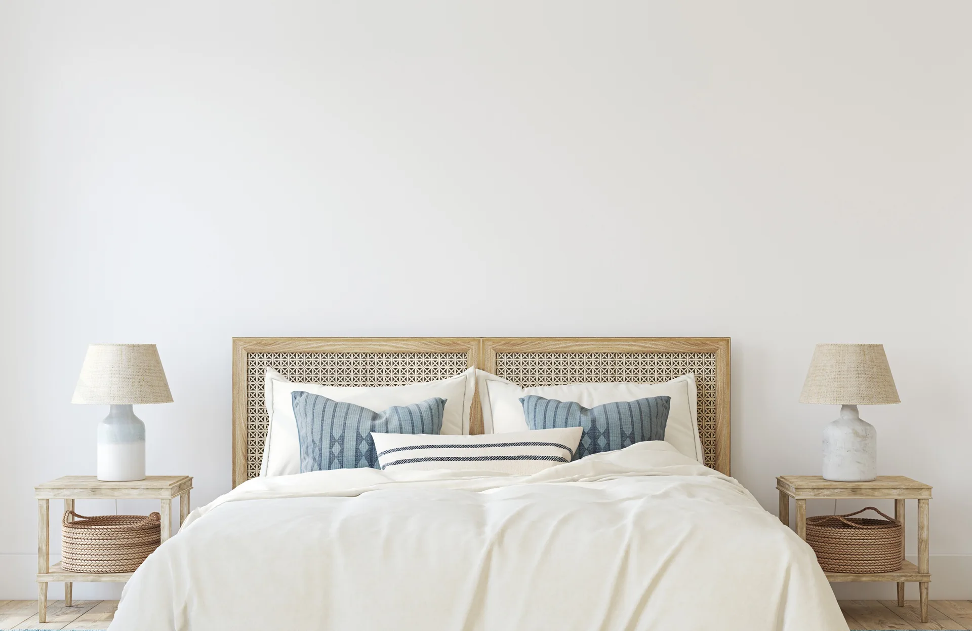 A symmetrical bedroom setup features a bed with a woven cane headboard, white bedding, blue patterned pillows, and matching wooden nightstands with lamps.
