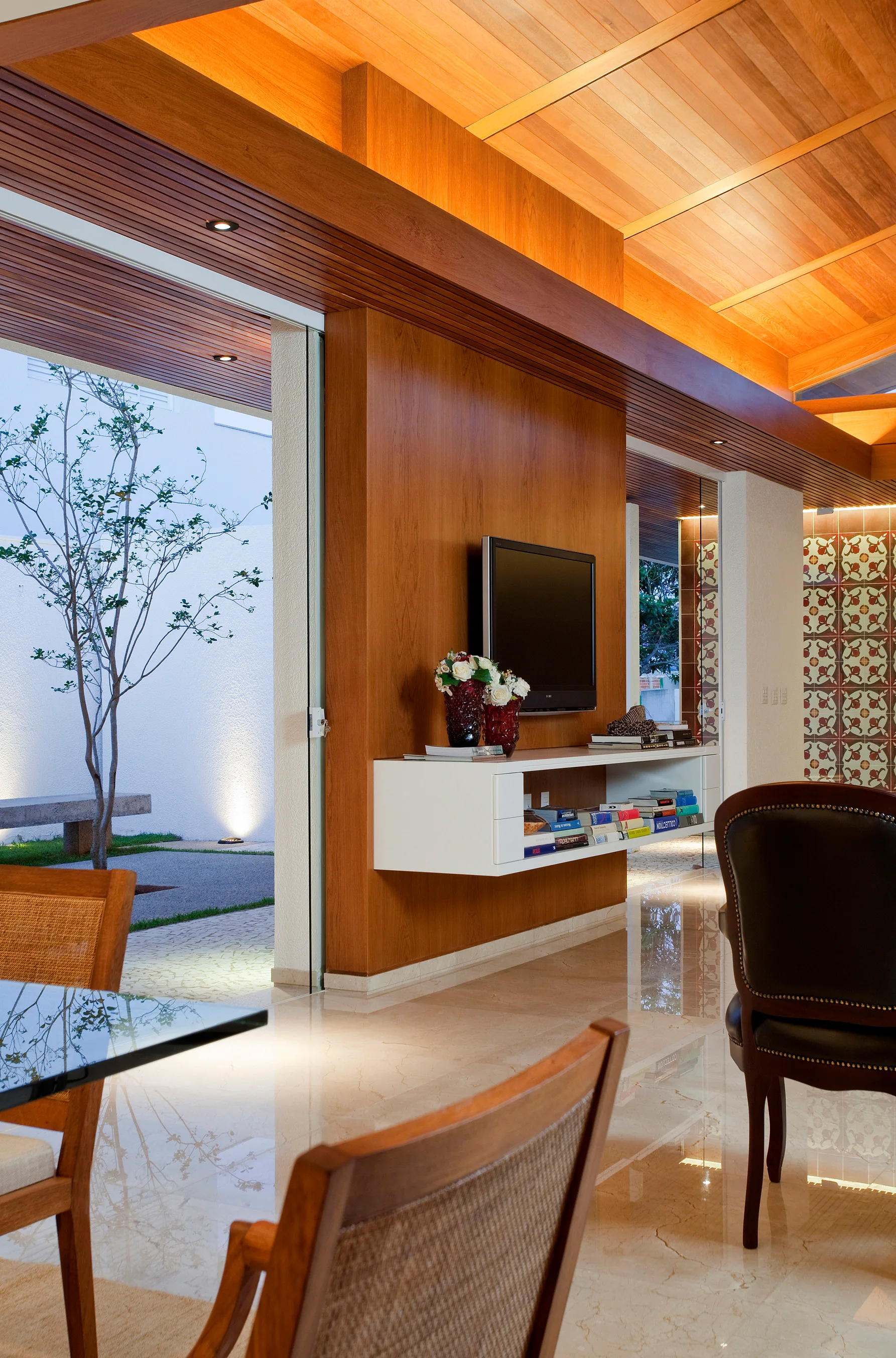 A modern living space features warm wood paneling on the walls and ceiling, a floating white media console, and highly polished stone floors.