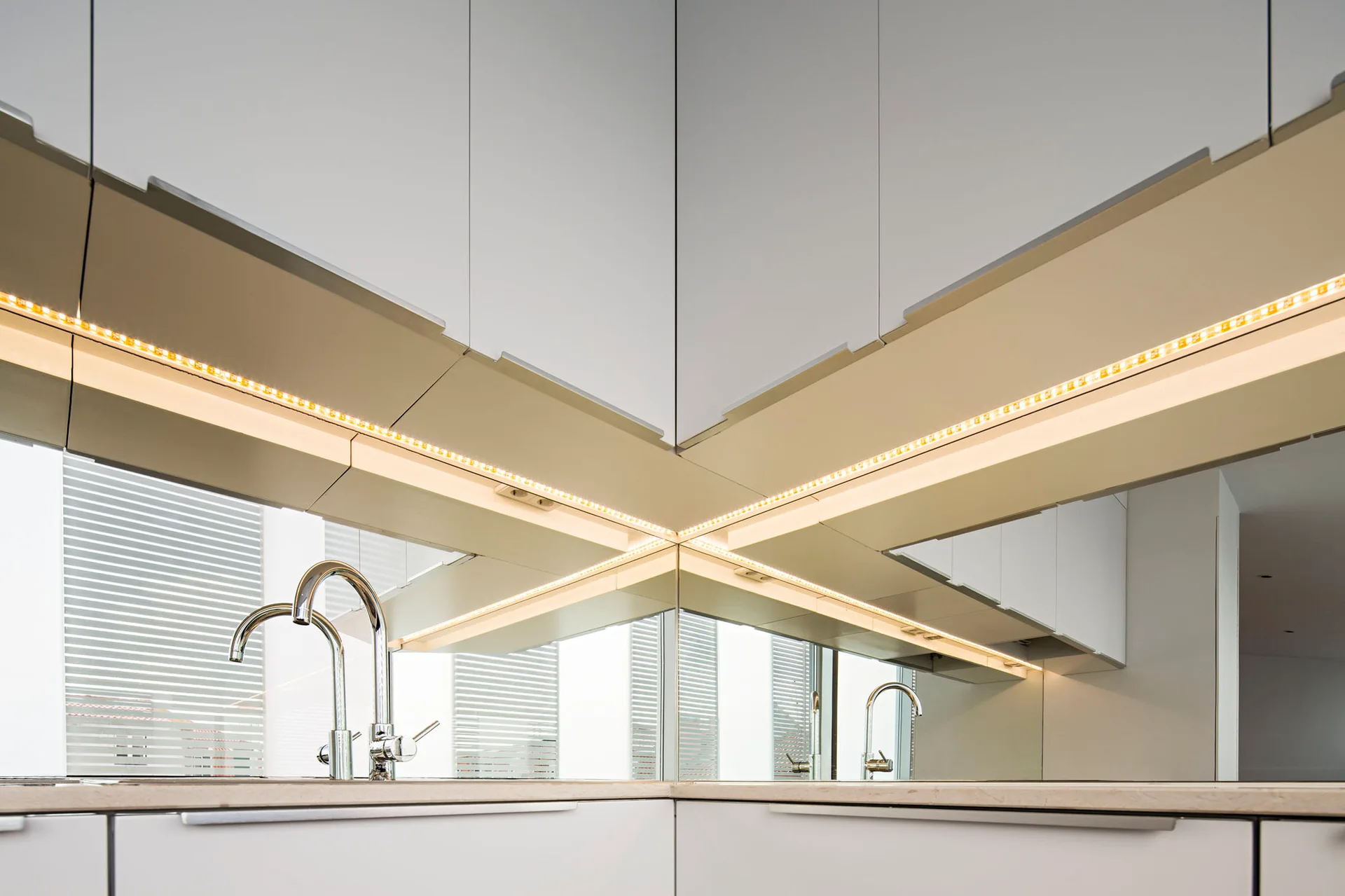 Matte white kitchen cabinetry featuring a corner mirrored backsplash, integrated LED under-cabinet strip lighting, and a polished chrome faucet.