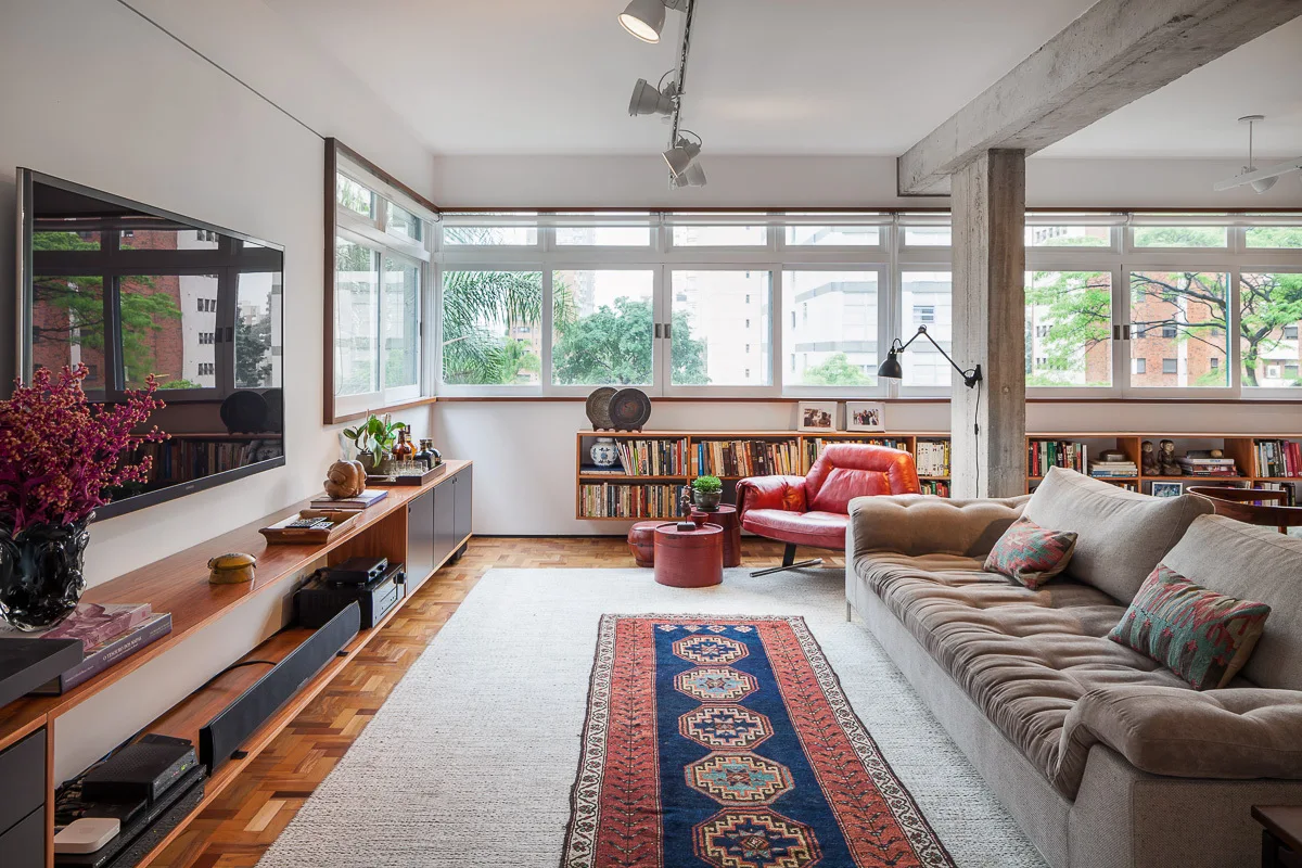 A living room features a tan sofa, an exposed concrete pillar, a red leather armchair, and a patterned runner rug over parquet flooring.